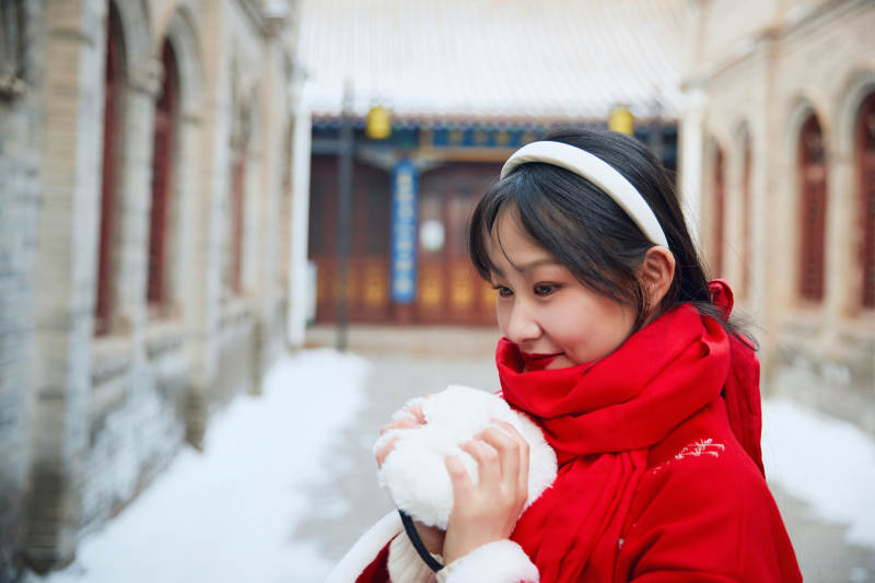 雪后在老城古巷穿着喜庆服饰的亚洲少女