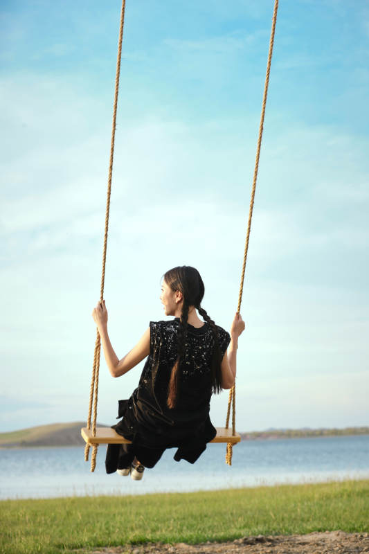 草原湖畔夕阳下荡秋千的亚洲少女