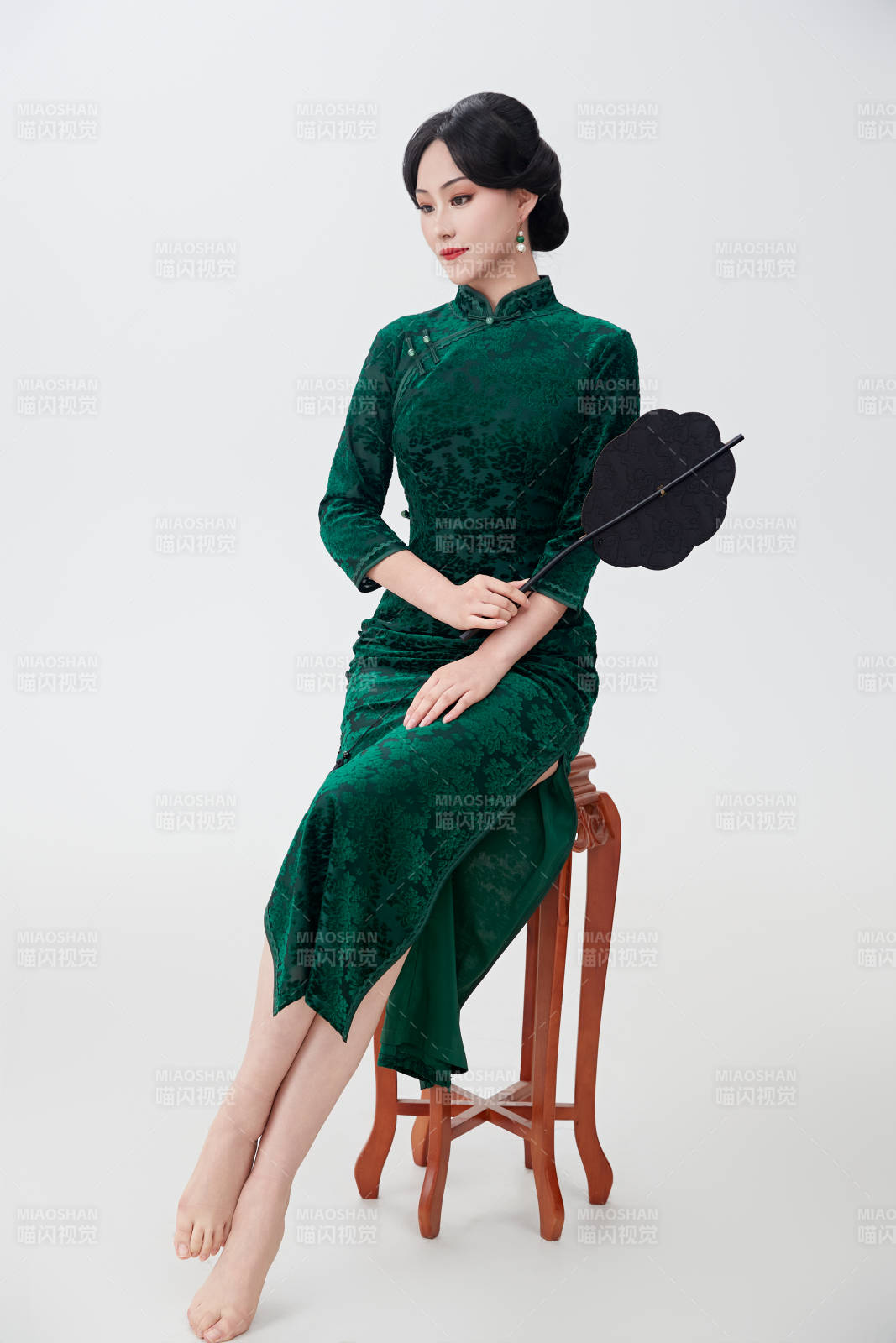 手拿紙扇身著中式旗袍坐在凳子上的美女