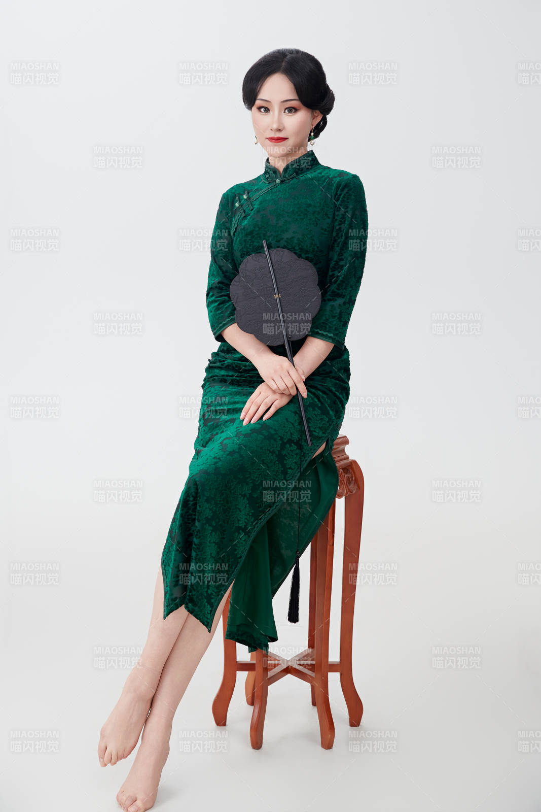 手拿紙扇身著中式旗袍坐在凳子上的美女