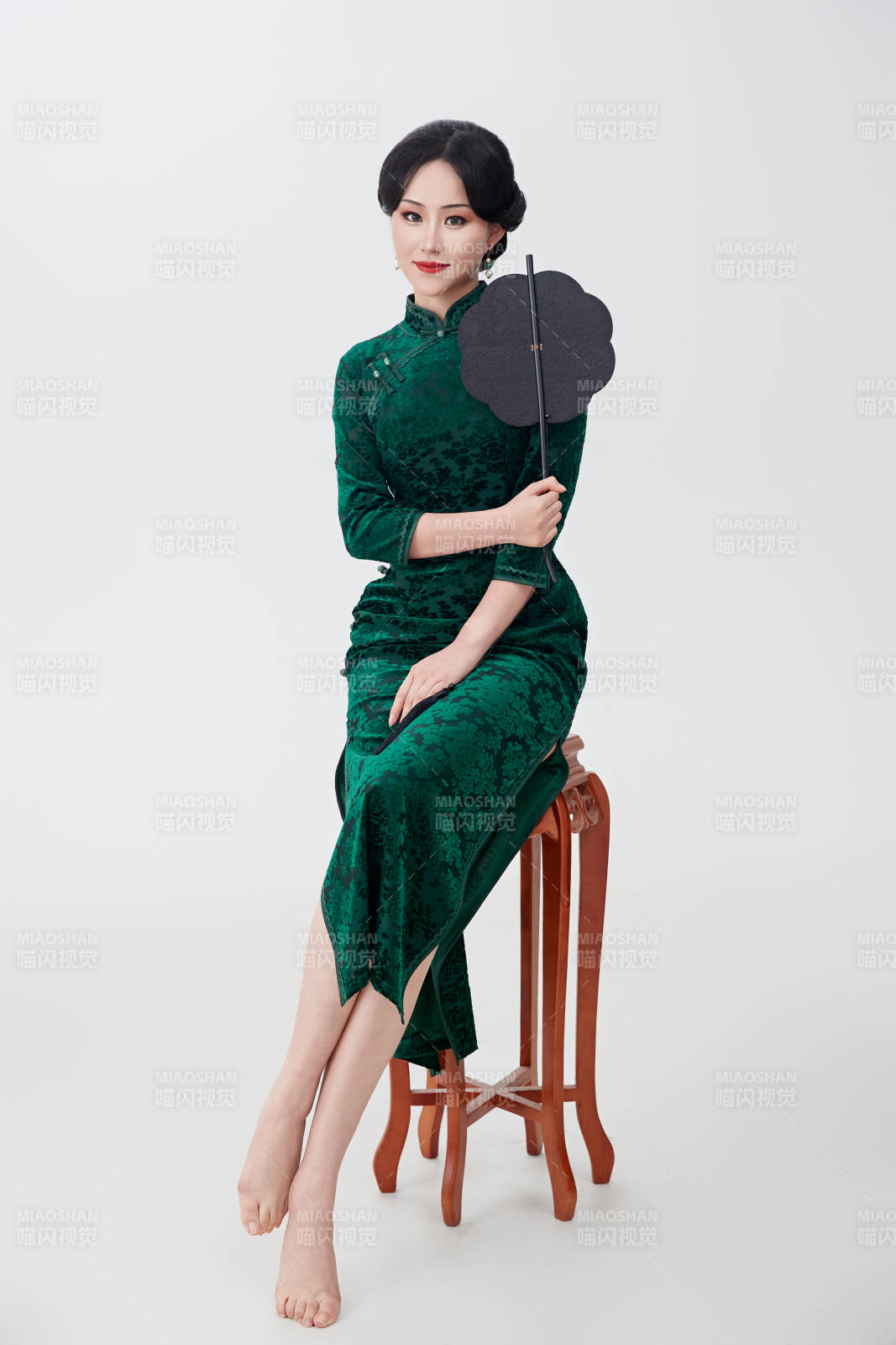 手拿紙扇身著中式旗袍坐在凳子上的美女