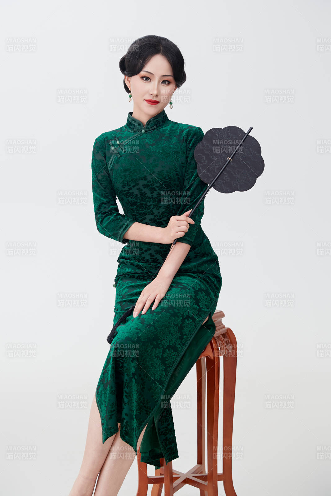 手拿纸扇身着中式旗袍坐在凳子上的美女