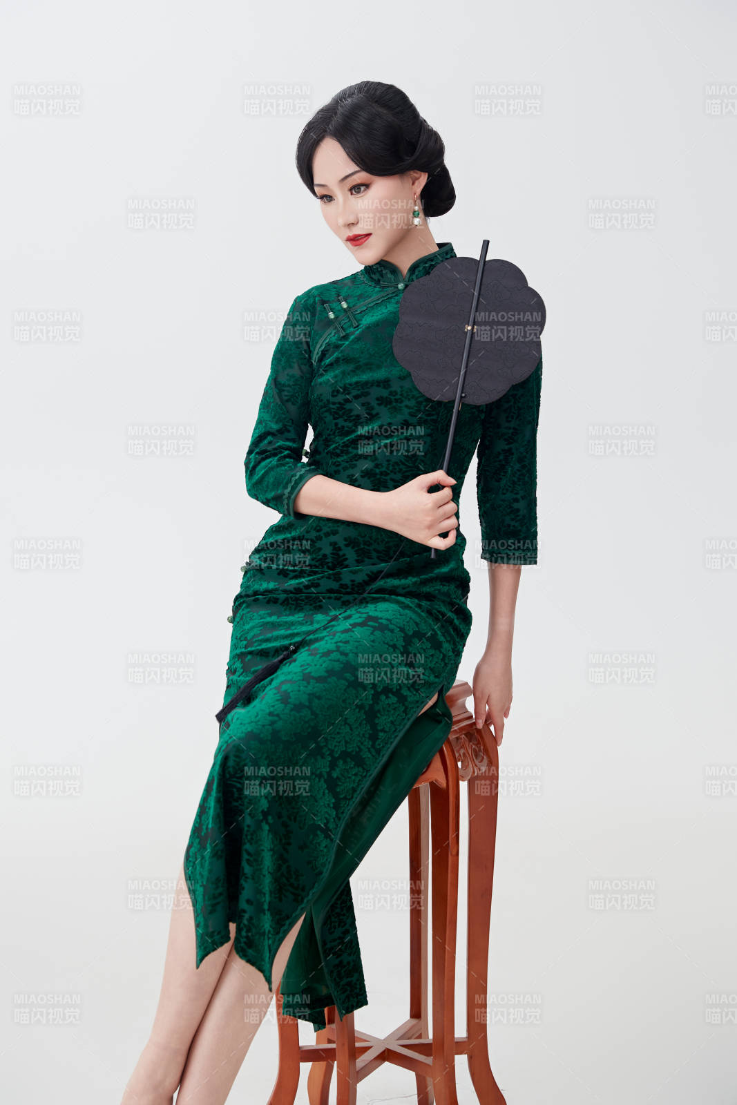 手拿紙扇身著中式旗袍坐在凳子上的美女