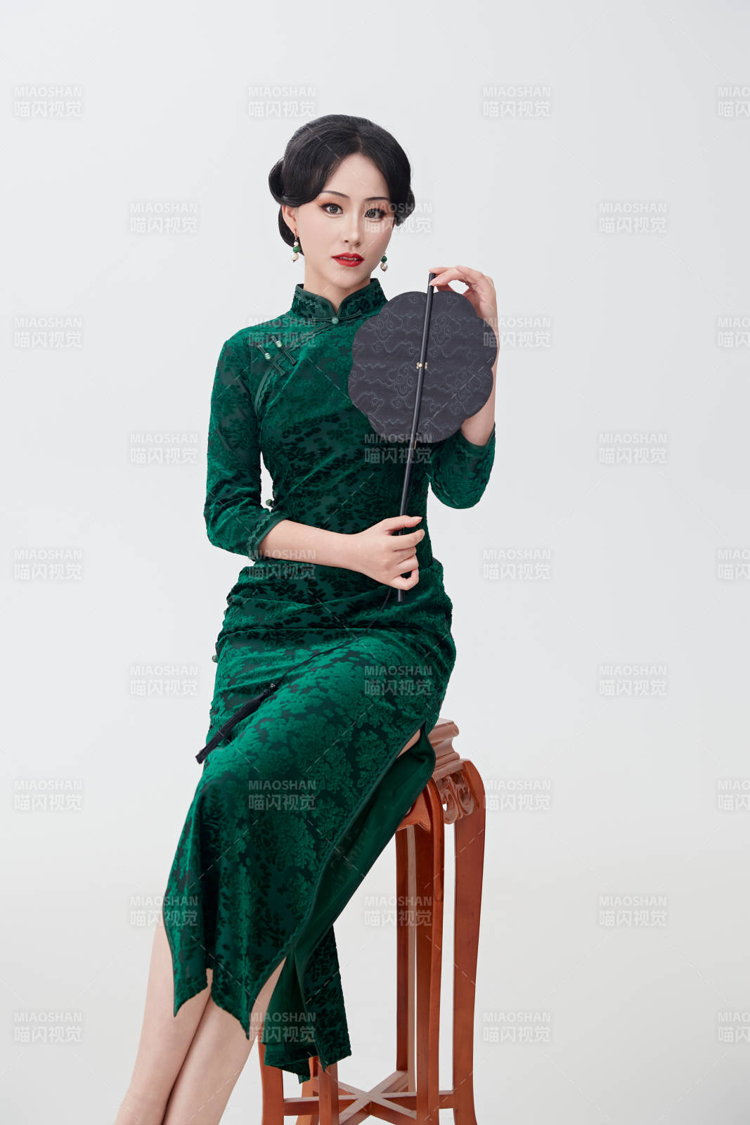 手拿紙扇身著中式旗袍坐在凳子上的美女