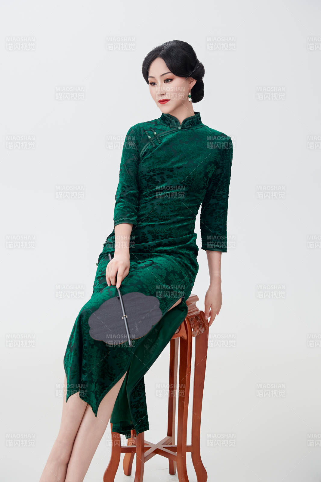 手拿紙扇身著中式旗袍坐在凳子上的美女