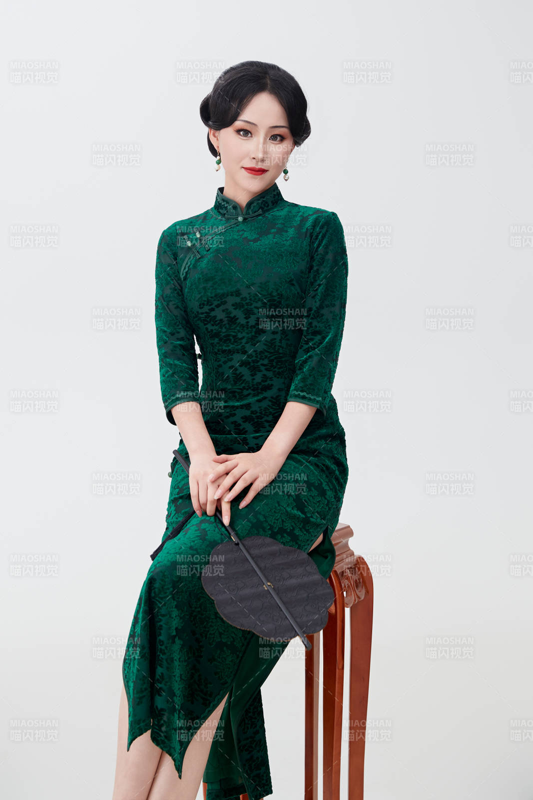 手拿紙扇身著中式旗袍坐在凳子上的美女
