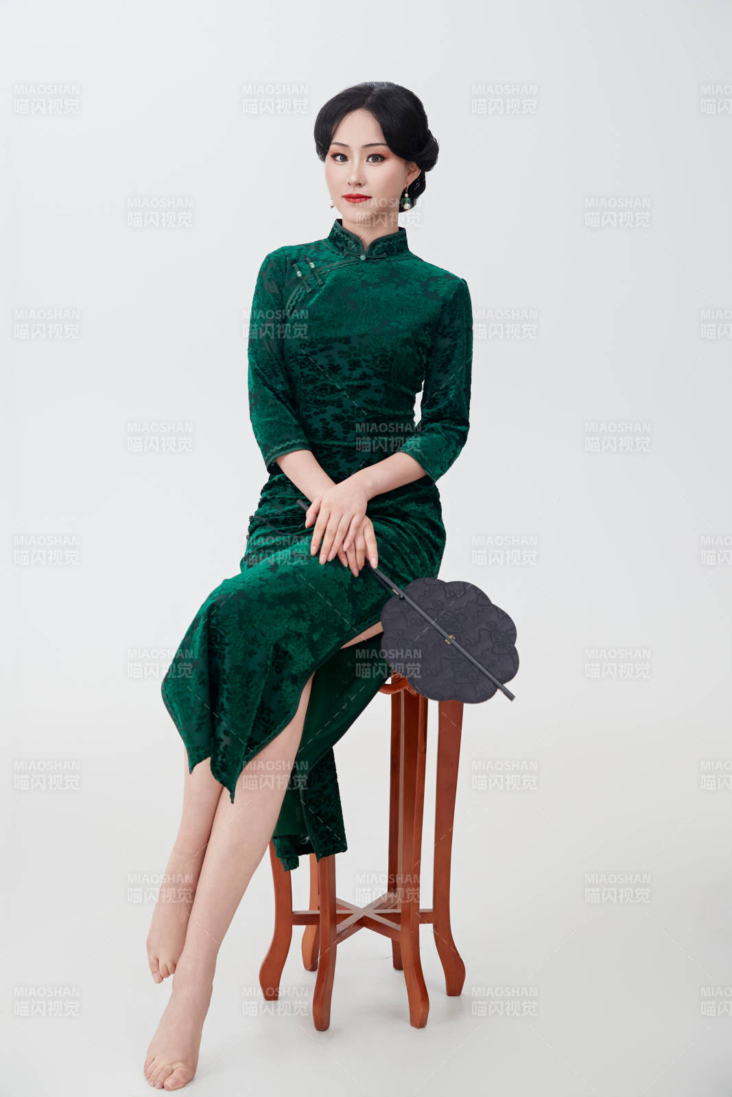 手拿紙扇身著中式旗袍坐在凳子上的美女