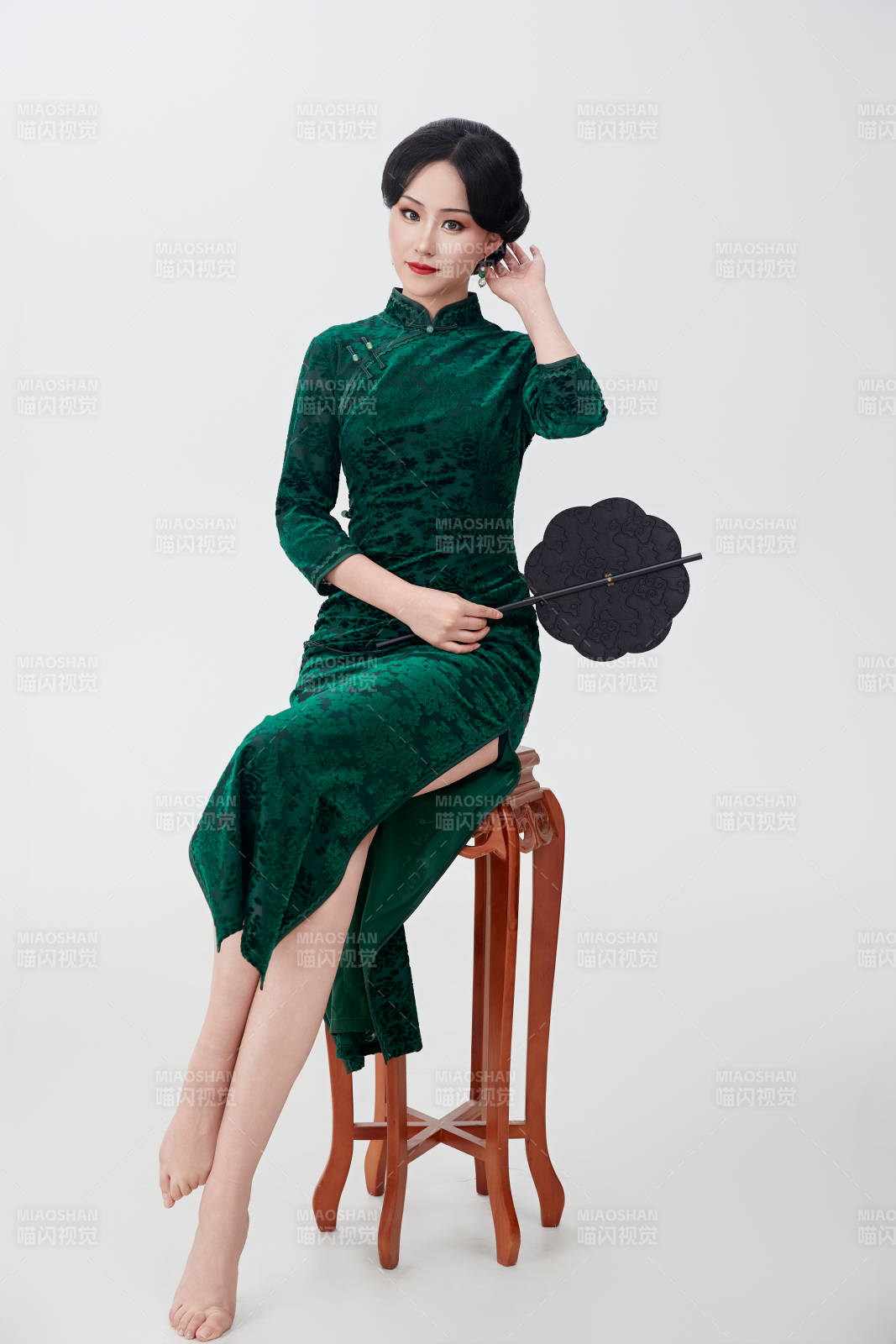 手拿紙扇身著中式旗袍坐在凳子上的美女