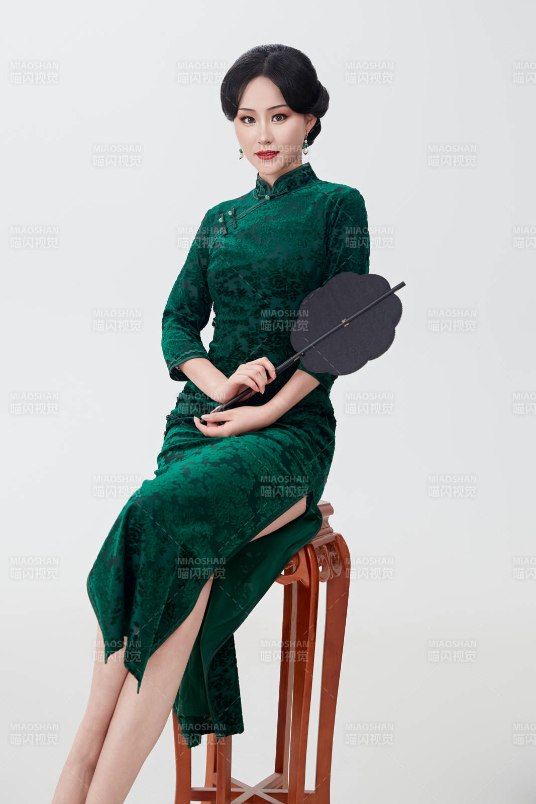手拿紙扇身著中式旗袍坐在凳子上的美女
