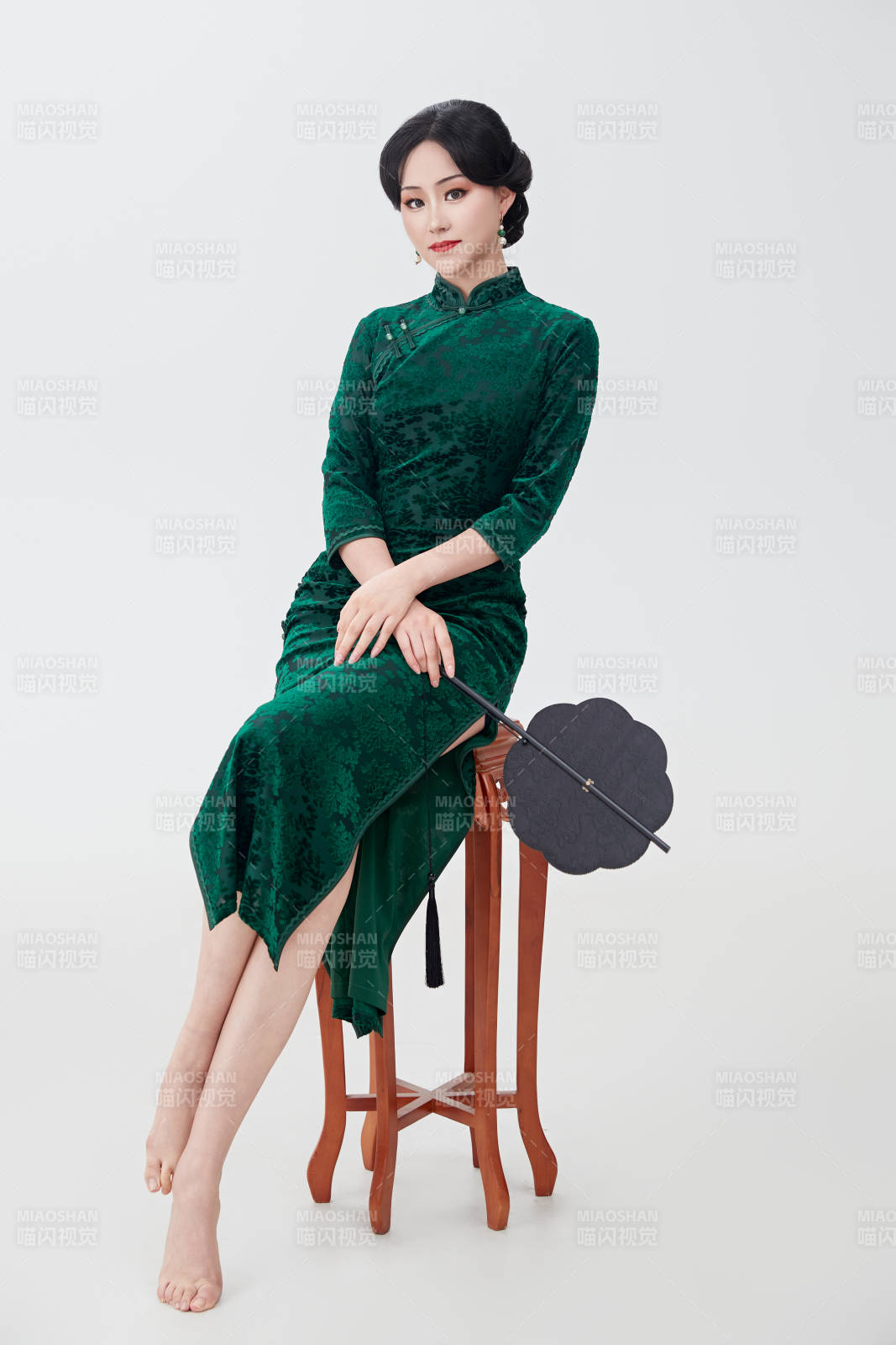手拿紙扇身著中式旗袍坐在凳子上的美女