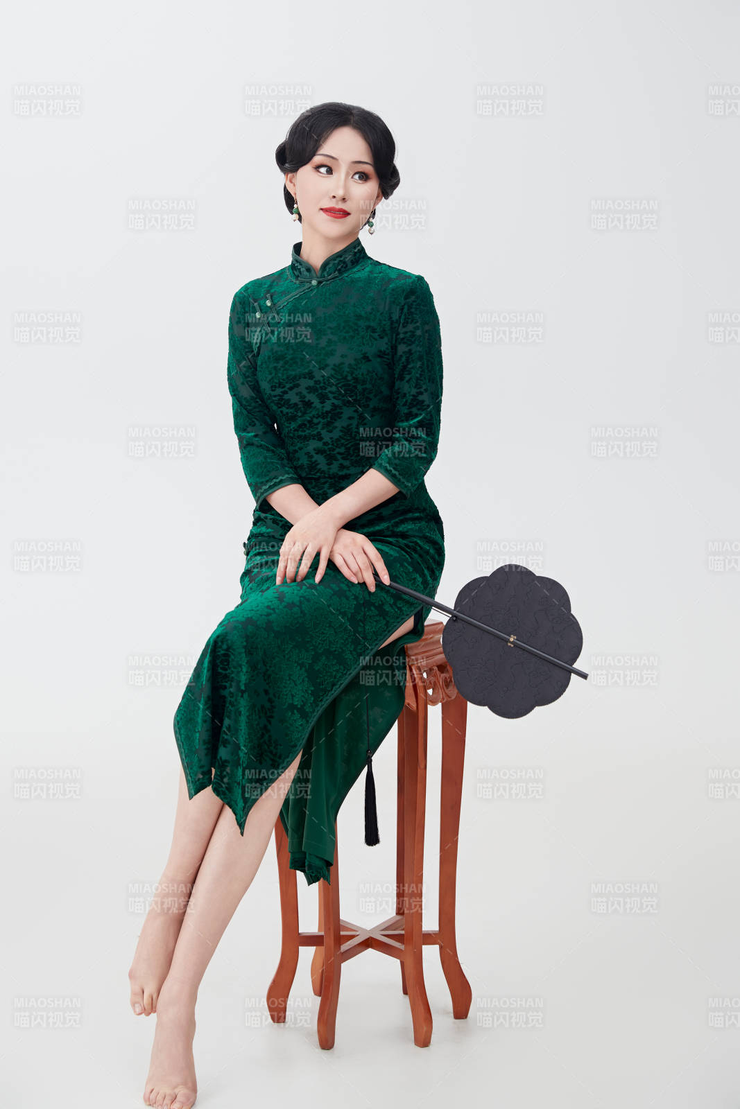 手拿纸扇身着中式旗袍坐在凳子上的美女