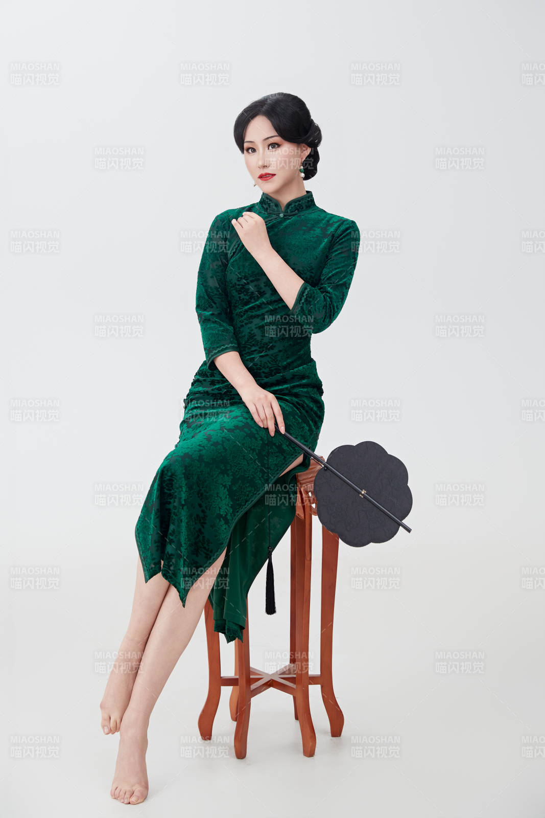 手拿紙扇身著中式旗袍坐在凳子上的美女