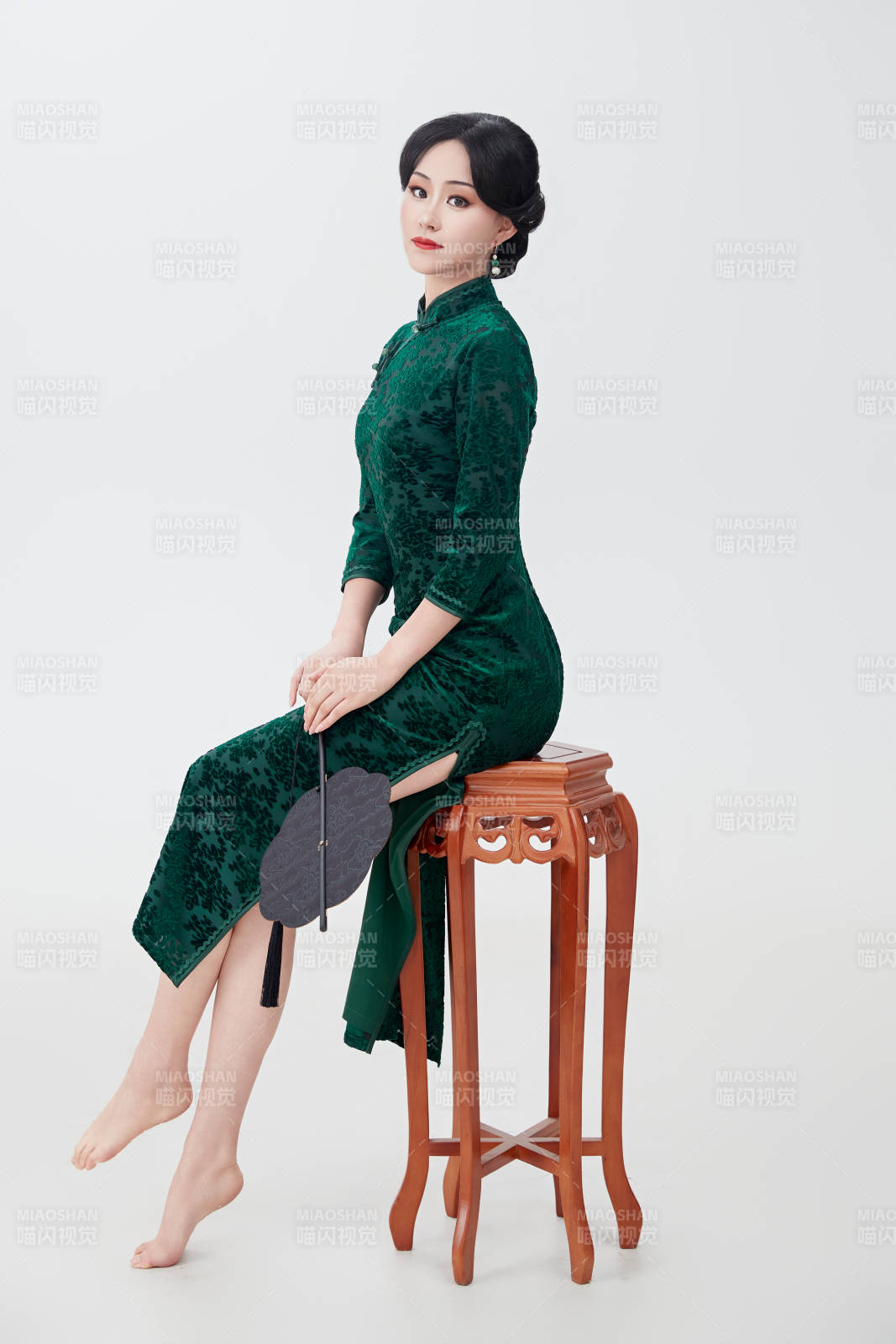 手拿紙扇身著中式旗袍坐在凳子上的美女