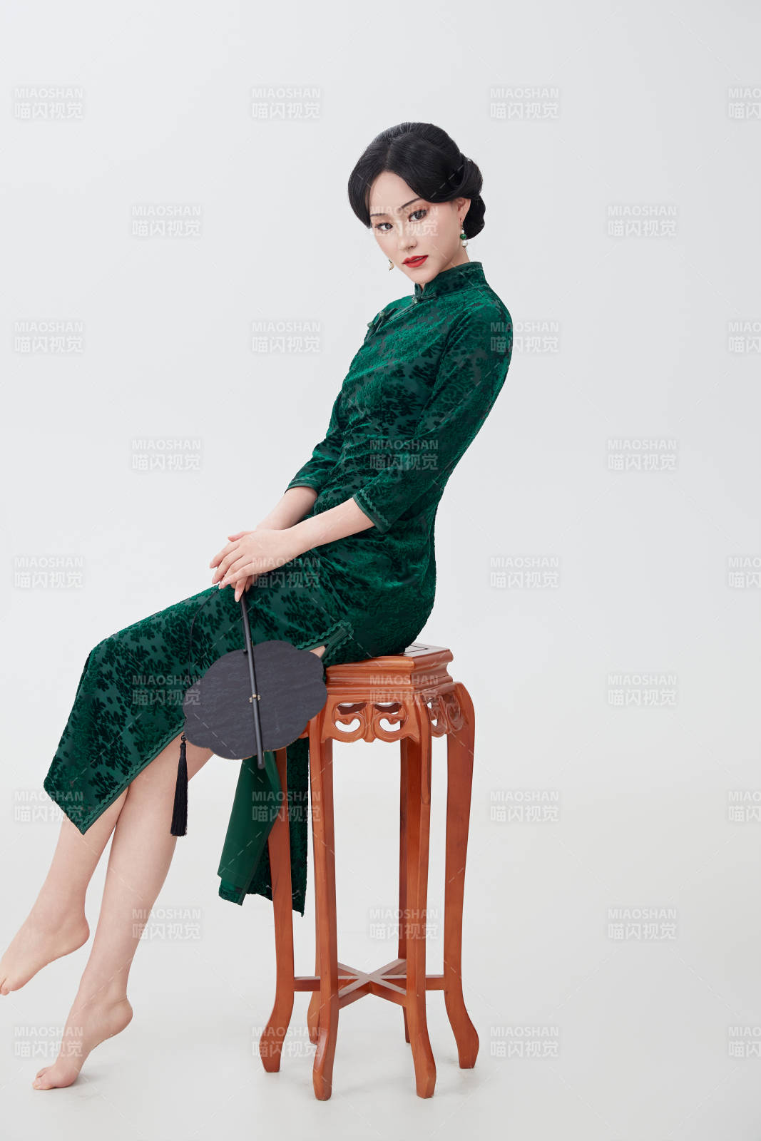 手拿纸扇身着中式旗袍坐在凳子上的美女