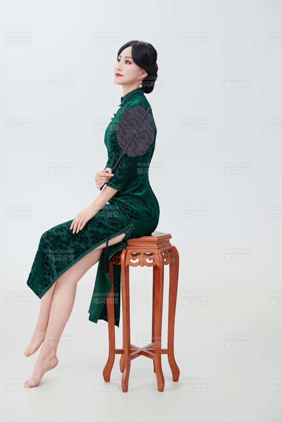 手拿紙扇身著中式旗袍坐在凳子上的美女