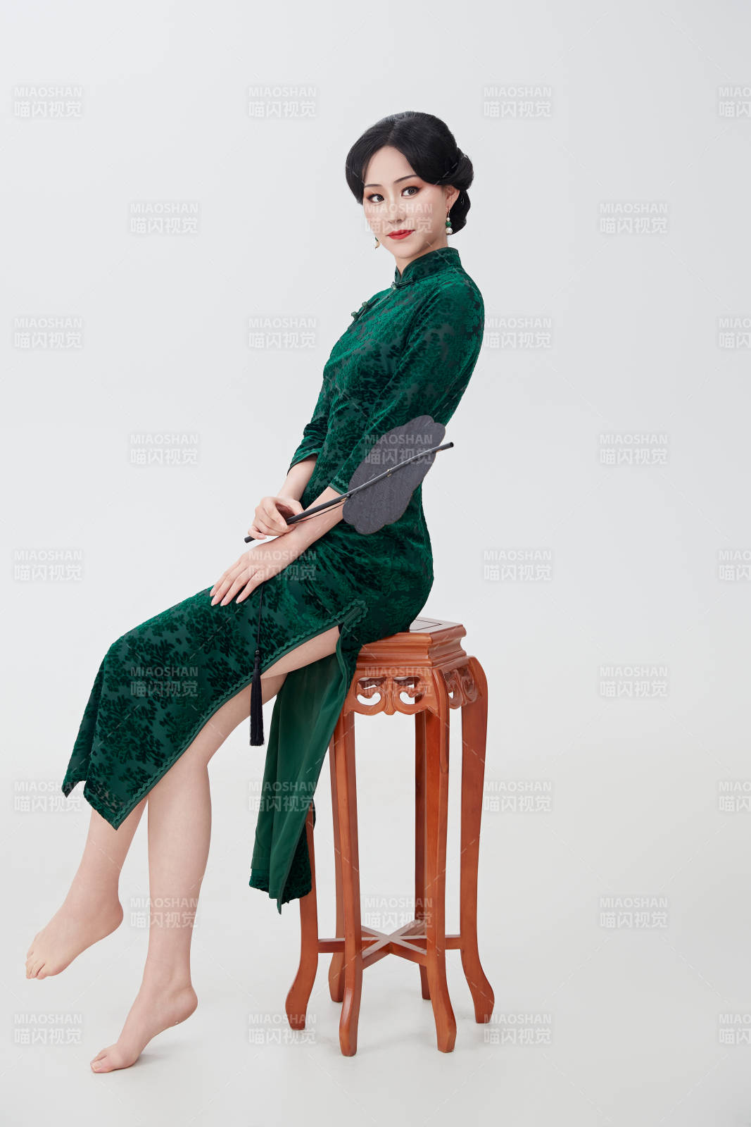 手拿紙扇身著中式旗袍坐在凳子上的美女