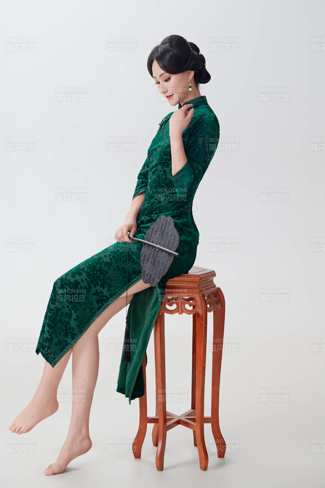 手拿紙扇身著中式旗袍坐在凳子上的美女