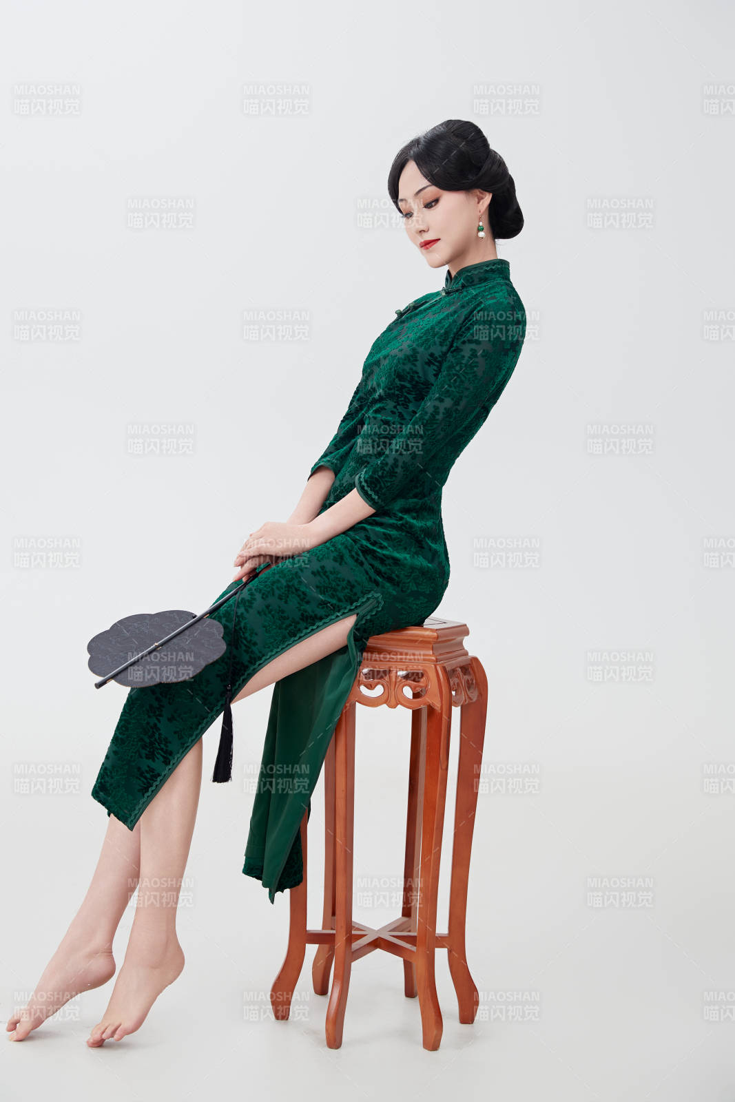 手拿纸扇身着中式旗袍坐在凳子上的美女