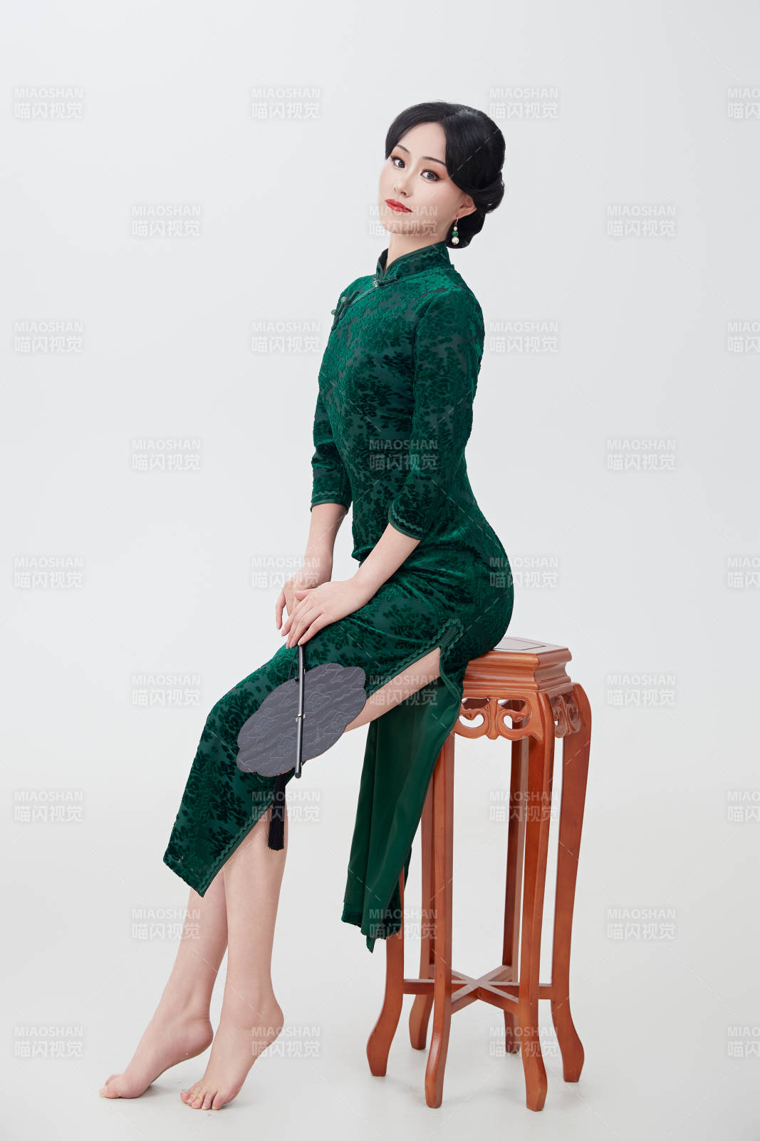 手拿紙扇身著中式旗袍坐在凳子上的美女