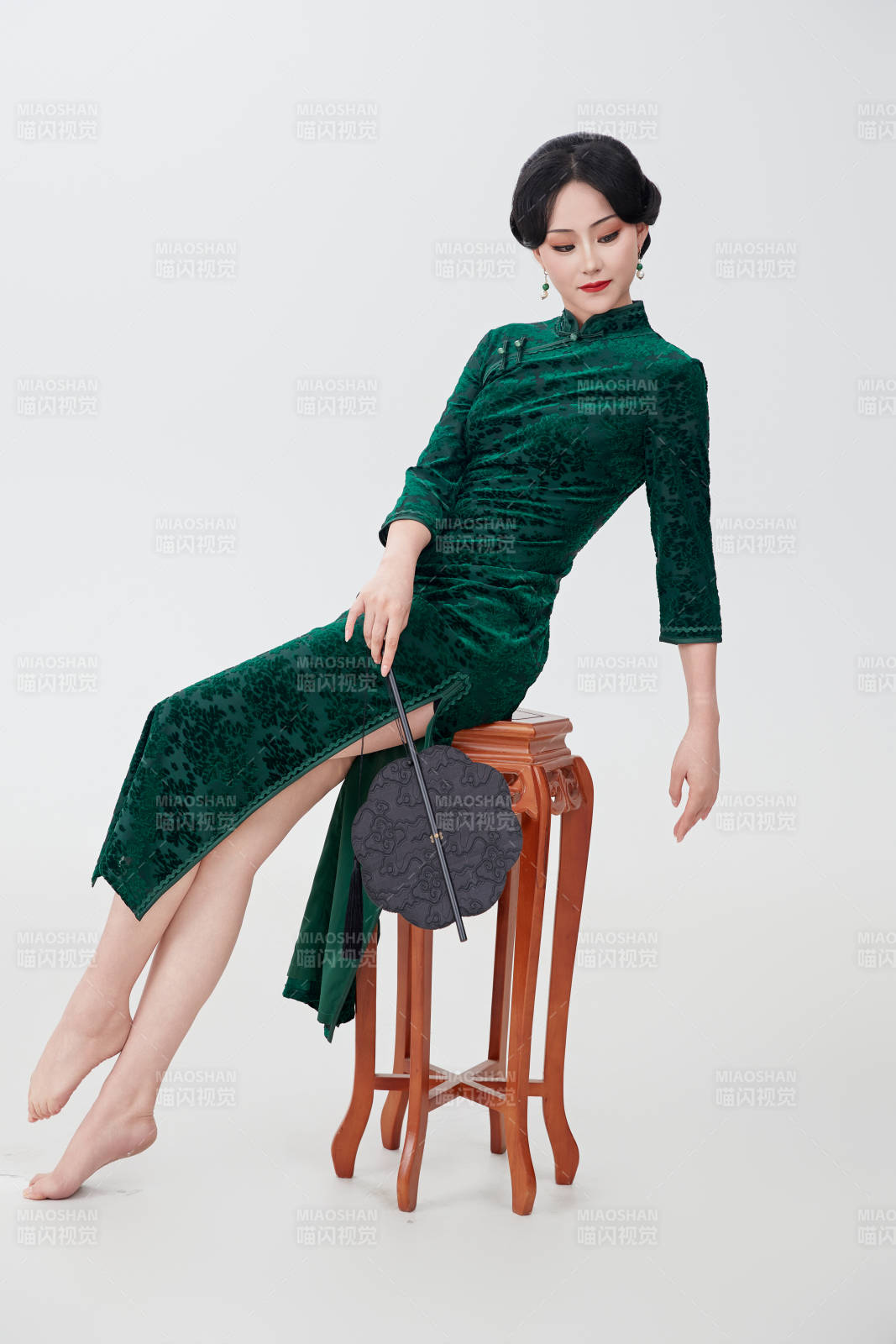 手拿紙扇身著中式旗袍坐在凳子上的美女