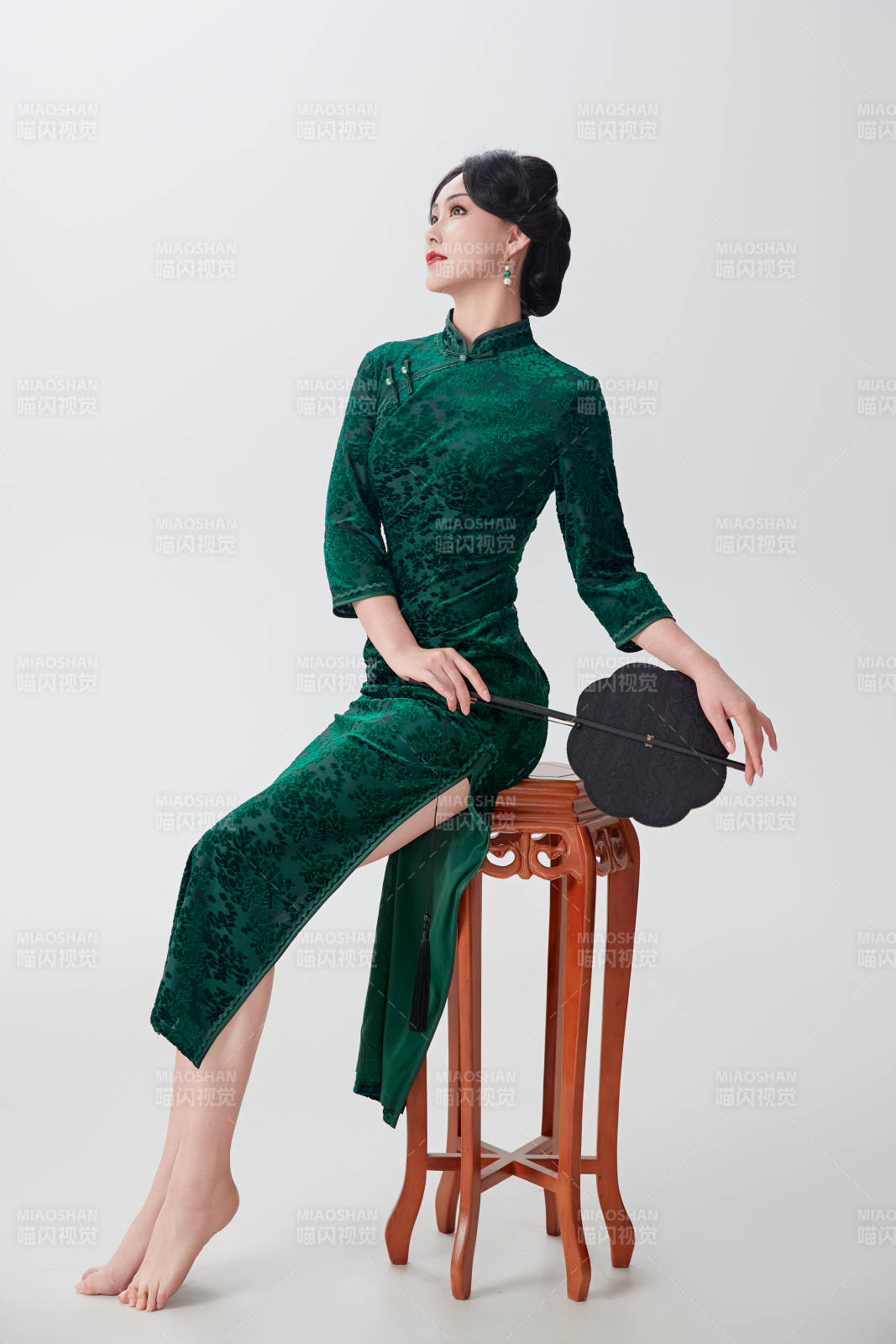 手拿紙扇身著中式旗袍坐在凳子上的美女