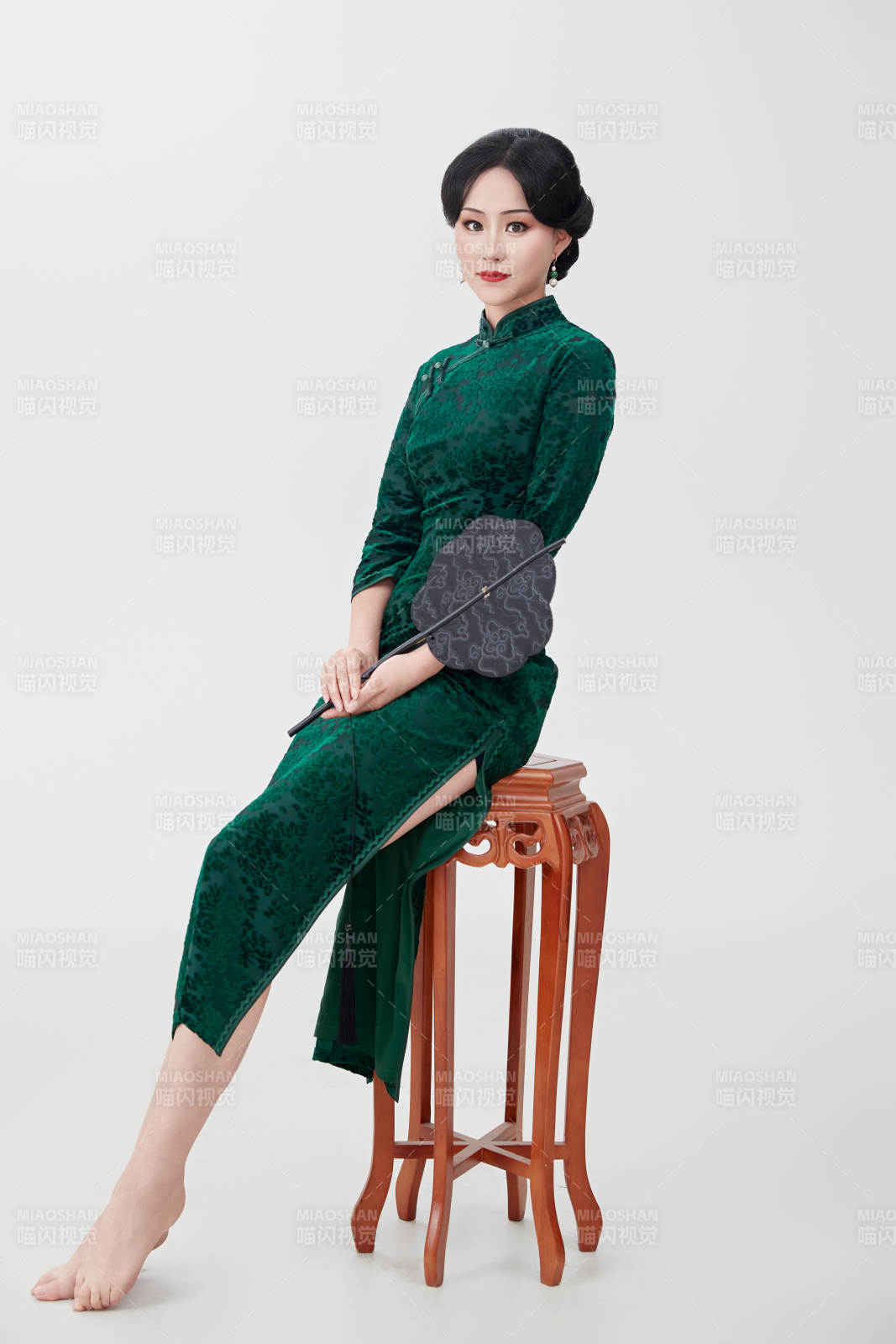 手拿紙扇身著中式旗袍坐在凳子上的美女