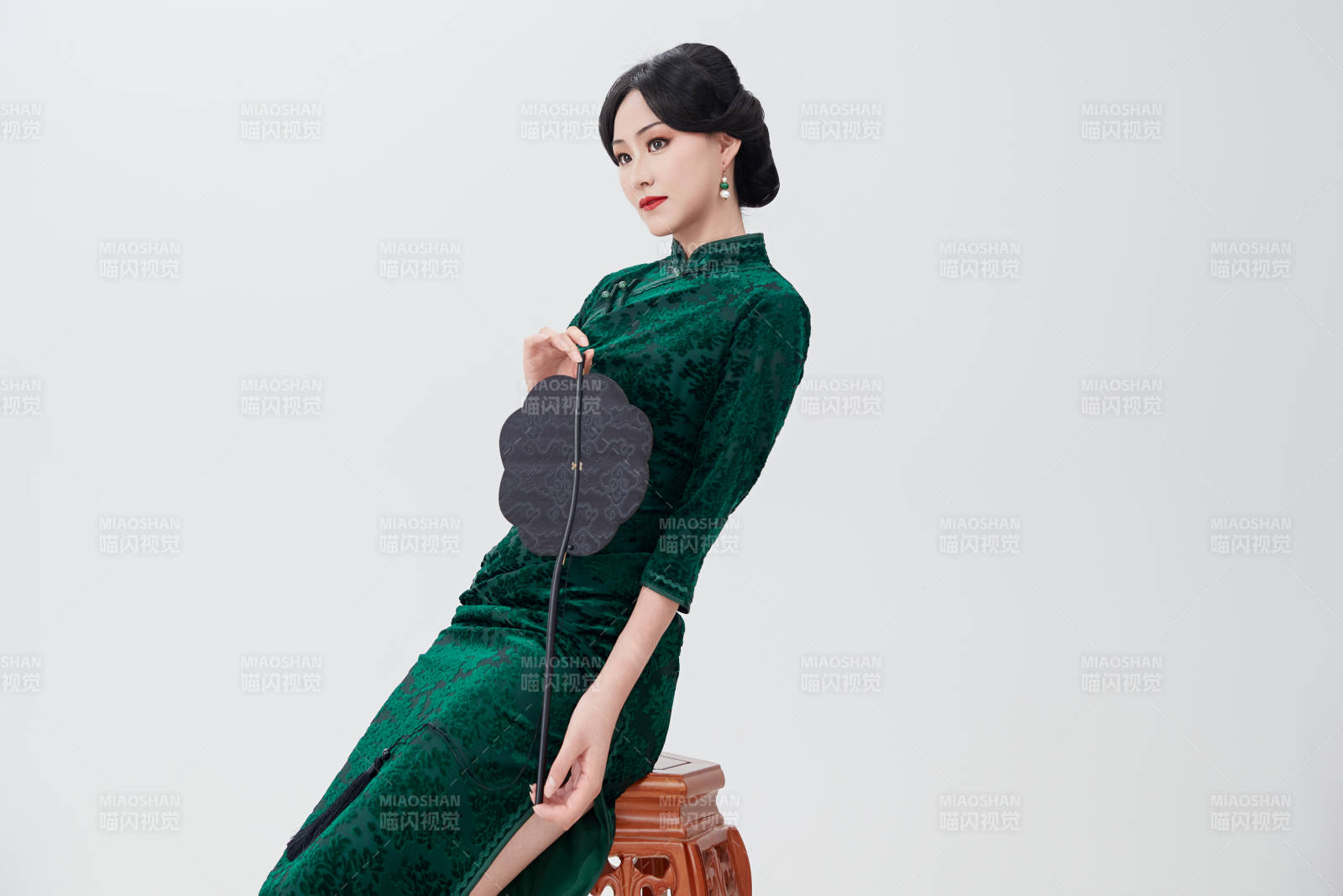 手拿紙扇身著中式旗袍坐在凳子上的美女