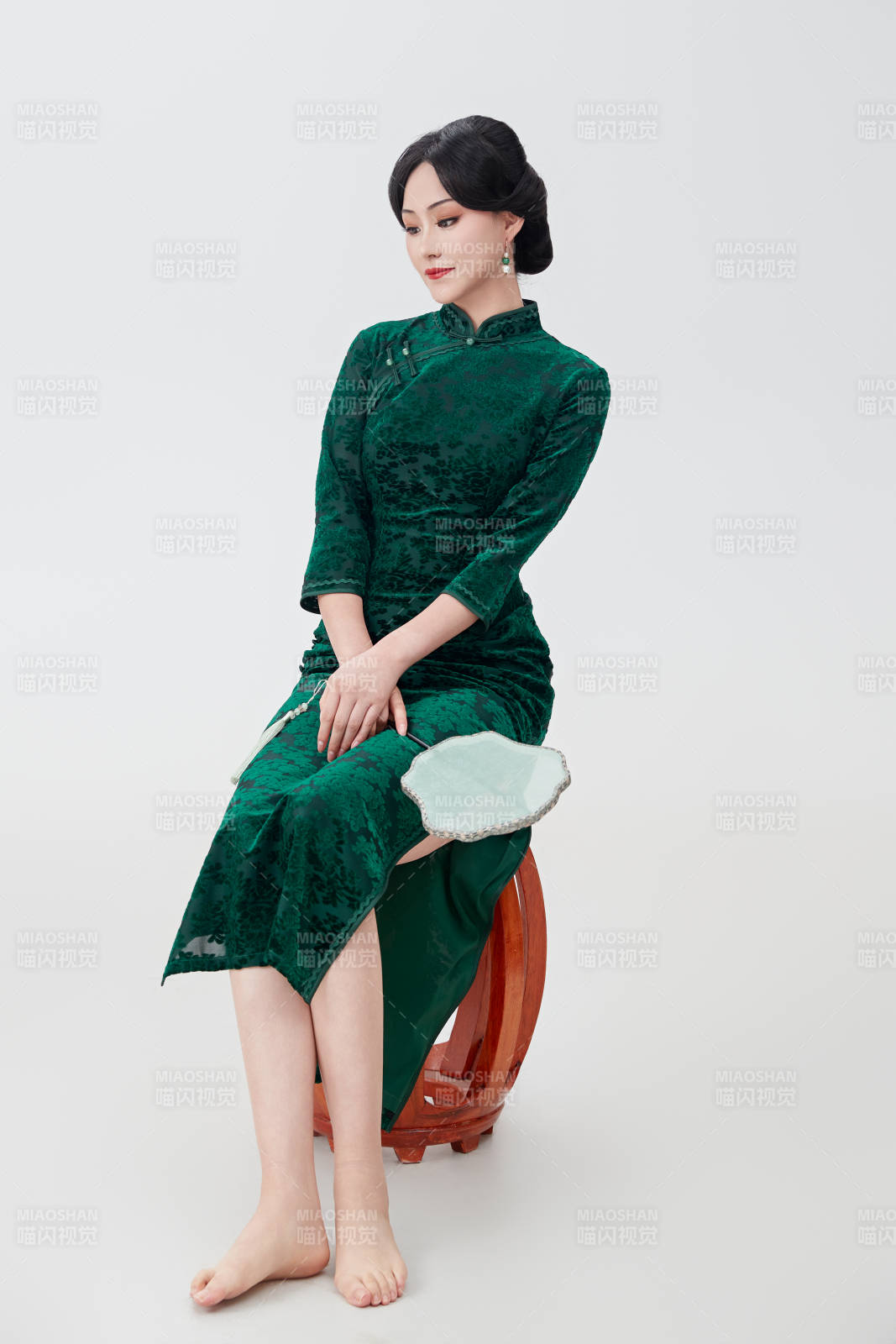 手拿紙扇身著中式旗袍坐在凳子上的美女