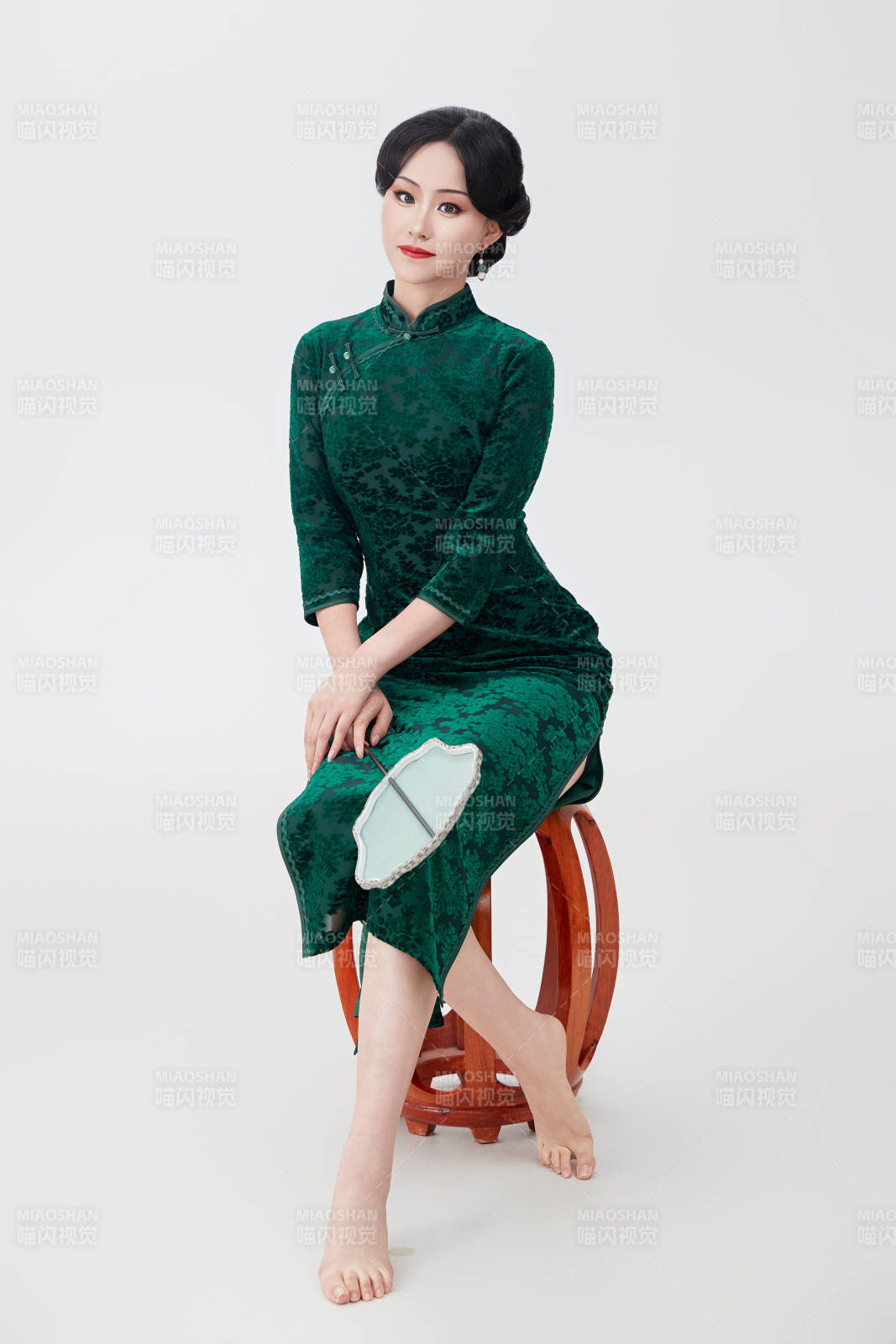 手拿紙扇身著中式旗袍坐在凳子上的美女