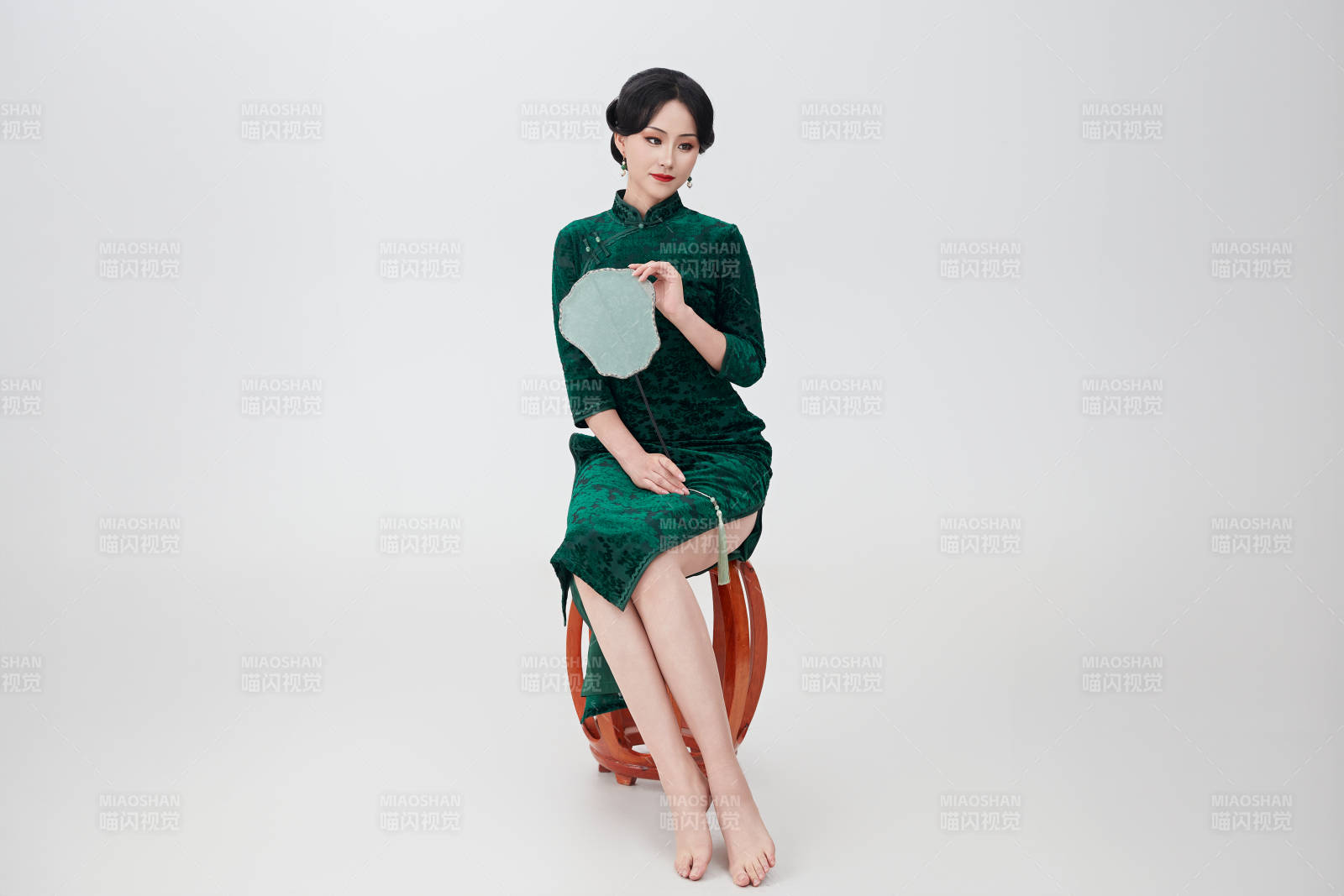 手拿纸扇身着中式旗袍坐在凳子上的美女