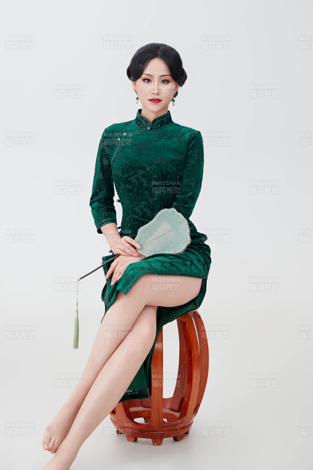 手拿紙扇身著中式旗袍坐在凳子上的美女