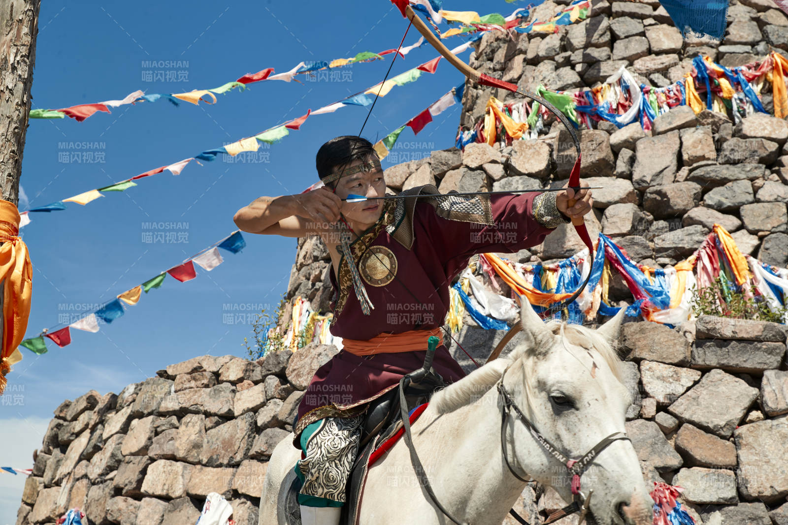 草原敖包前騎馬拉弓射箭的蒙古弓箭手