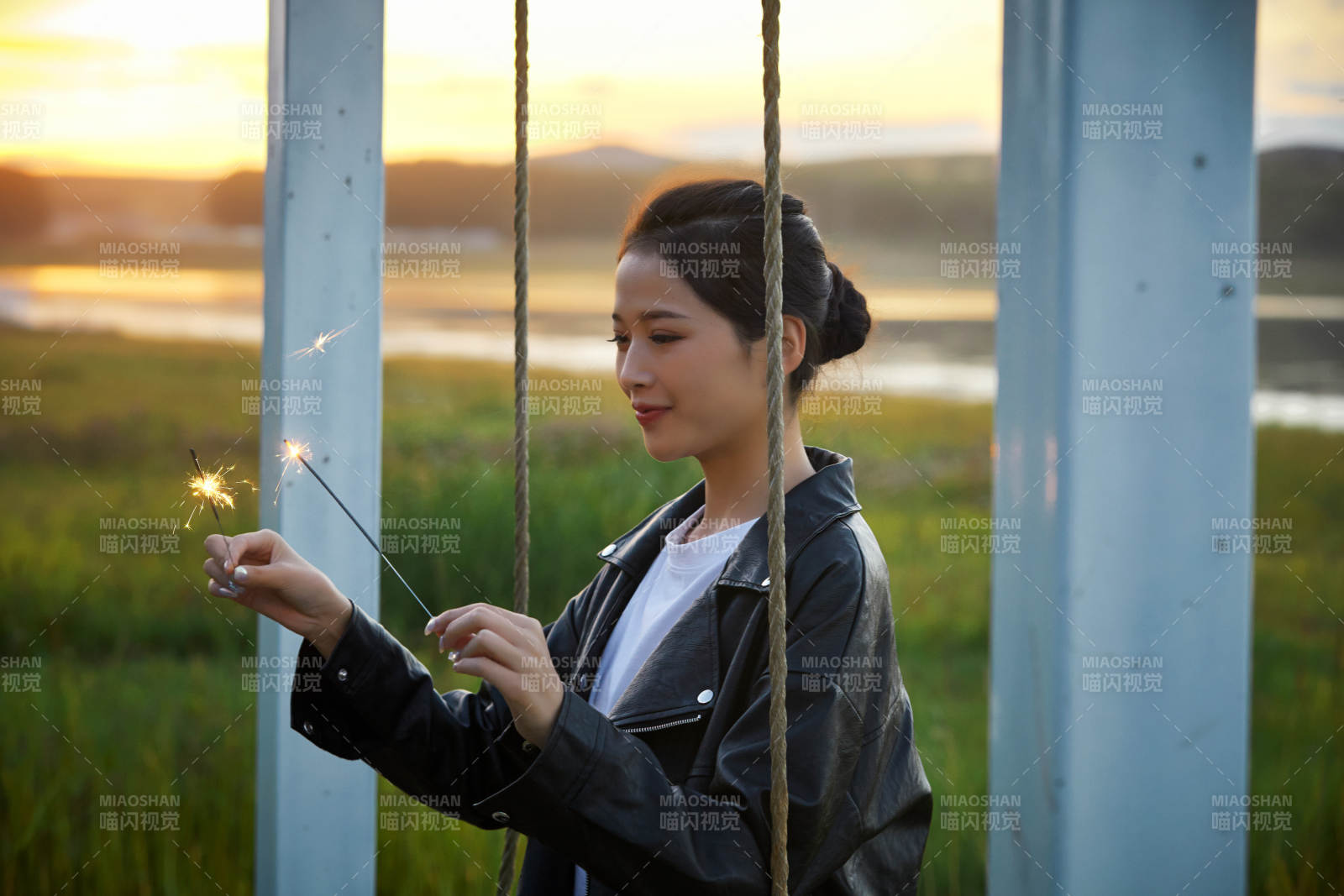 夕陽下湖畔秋千上燃放仙女棒的可愛少女