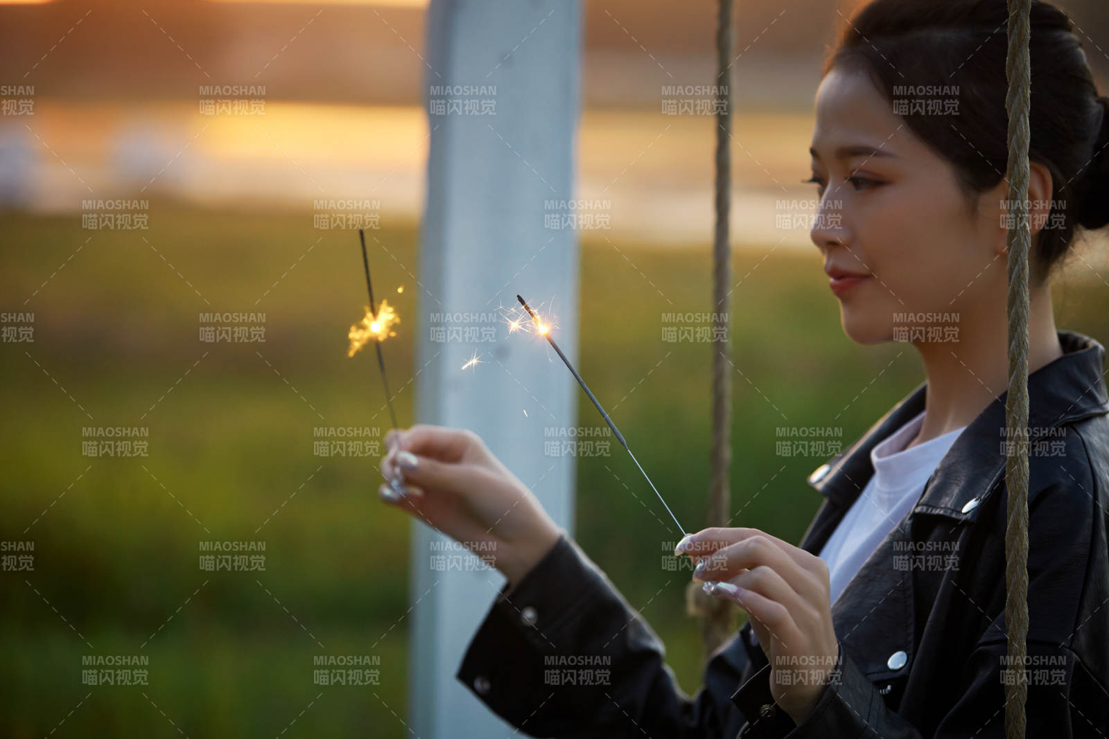 夕陽下湖畔秋千上燃放仙女棒的可愛少女