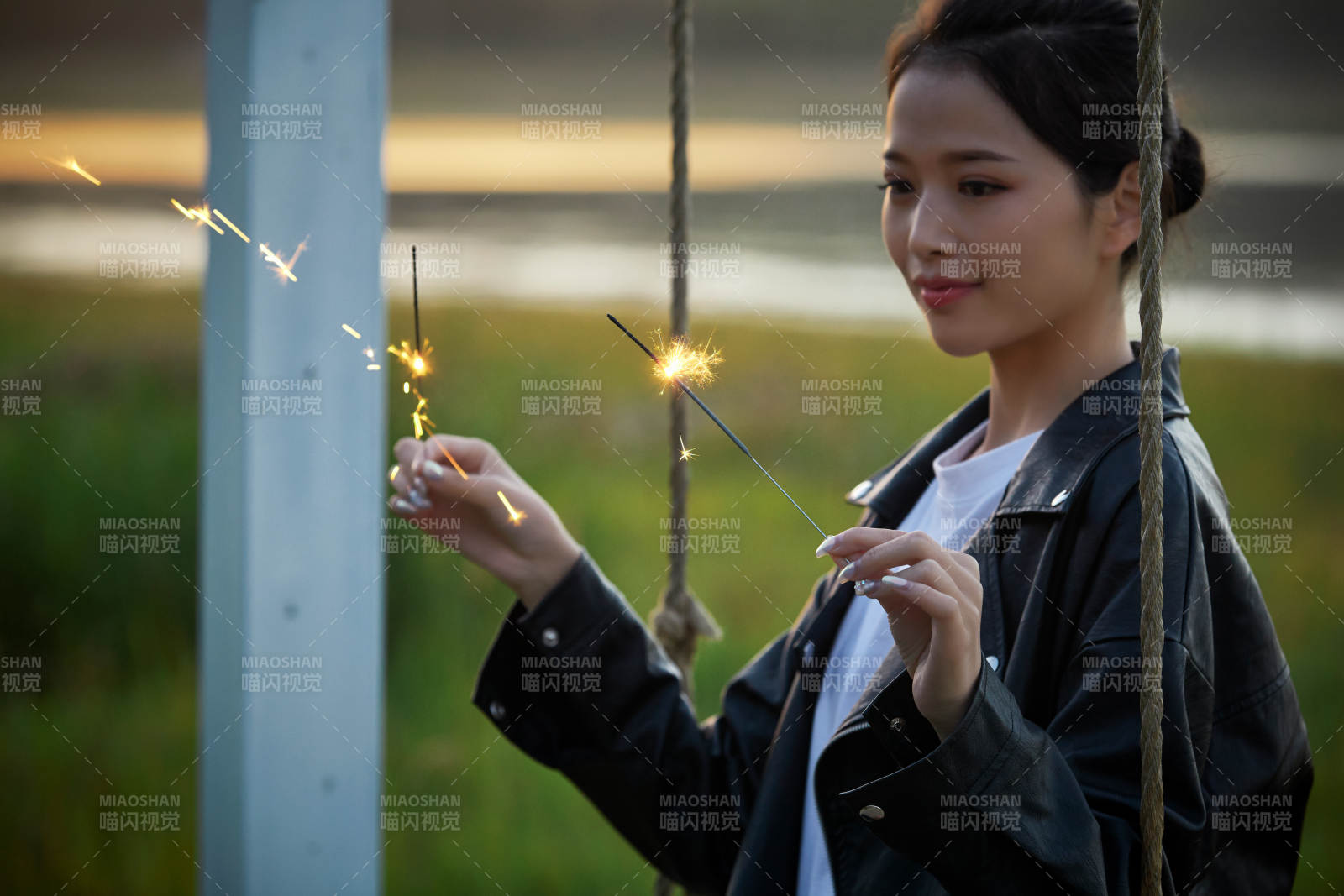 夕陽下湖畔秋千上燃放仙女棒的可愛少女