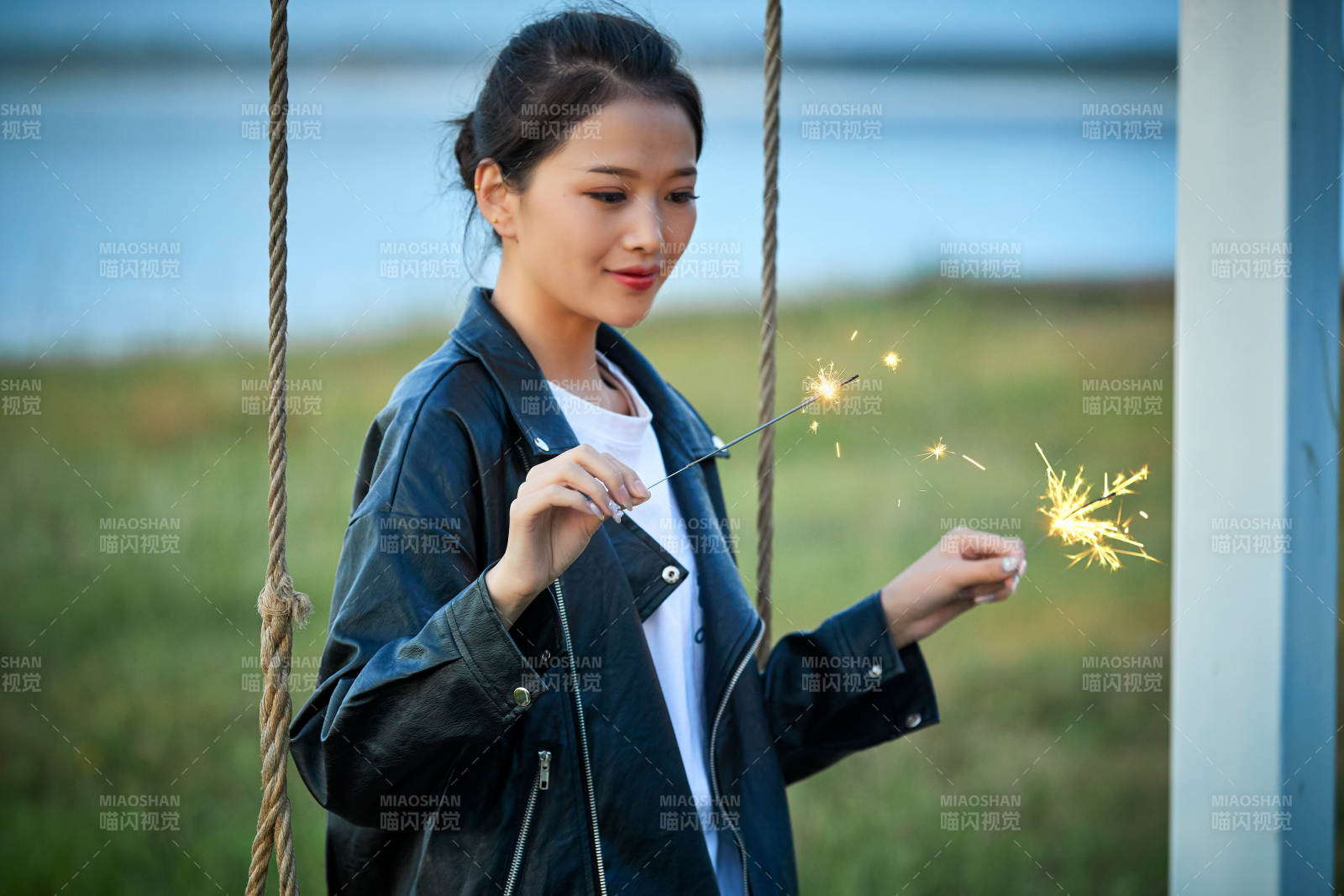 夕陽下湖畔秋千上燃放仙女棒的可愛少女