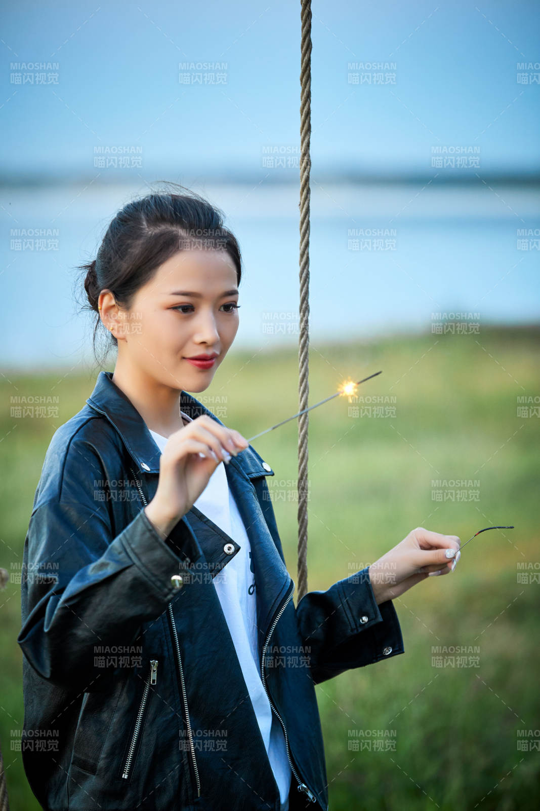 夕陽下湖畔秋千上燃放仙女棒的可愛少女