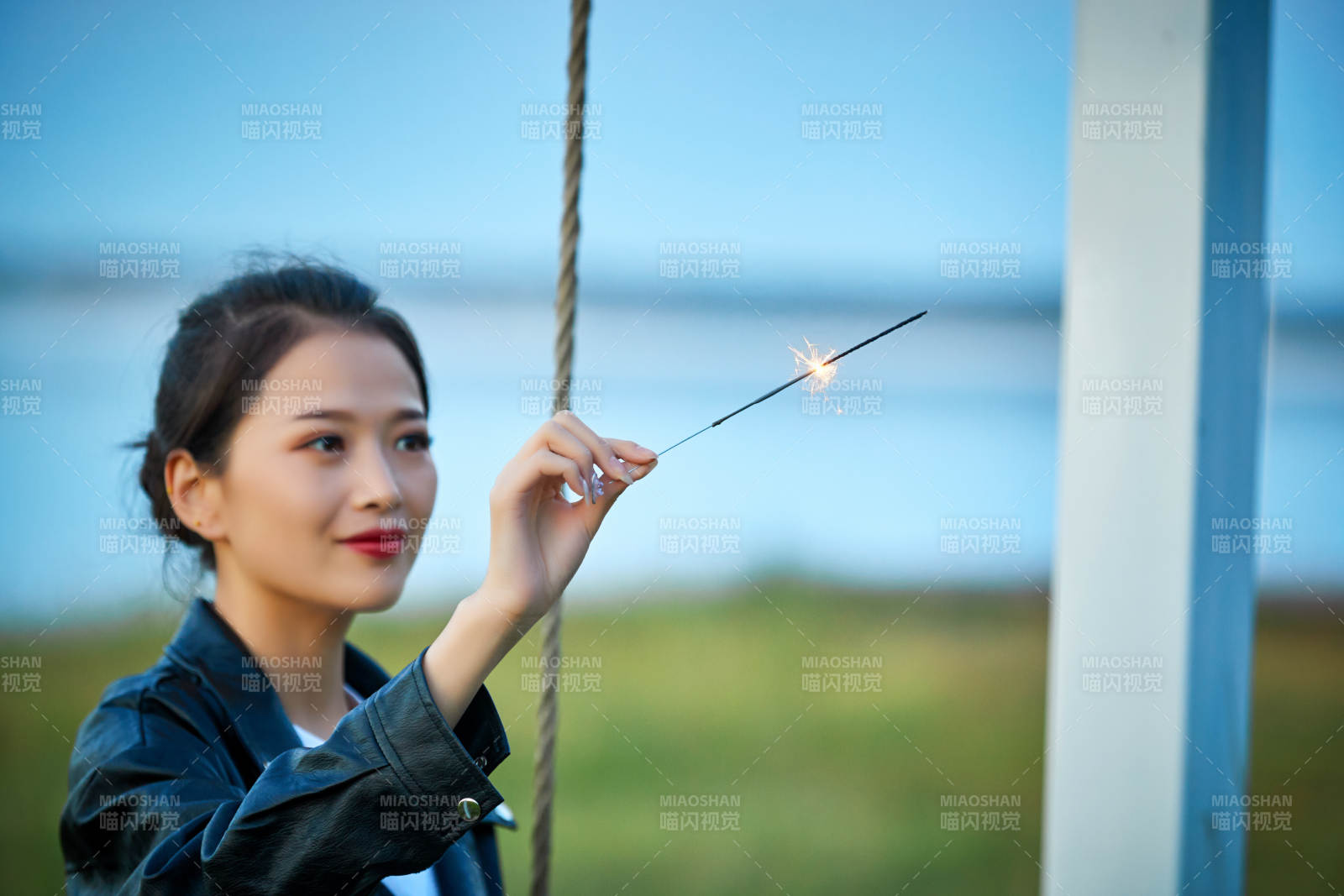 夕陽下湖畔秋千上燃放仙女棒的可愛少女