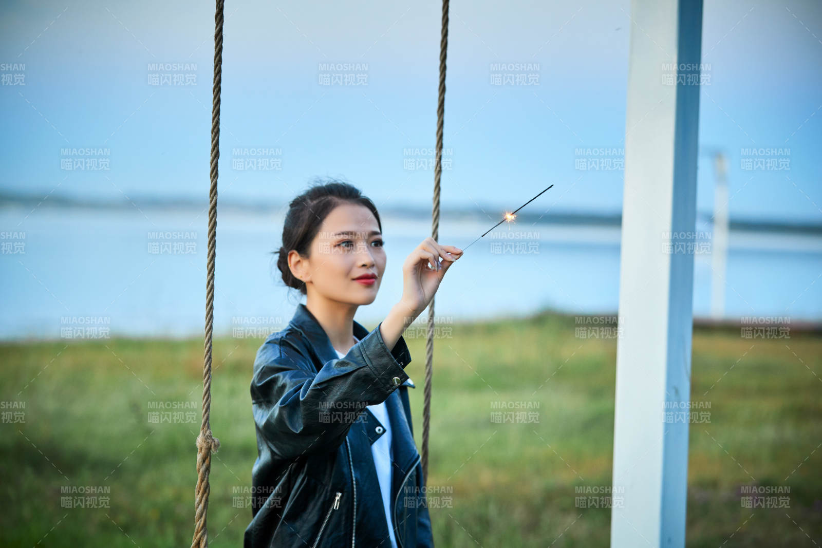 夕陽下湖畔秋千上燃放仙女棒的可愛少女