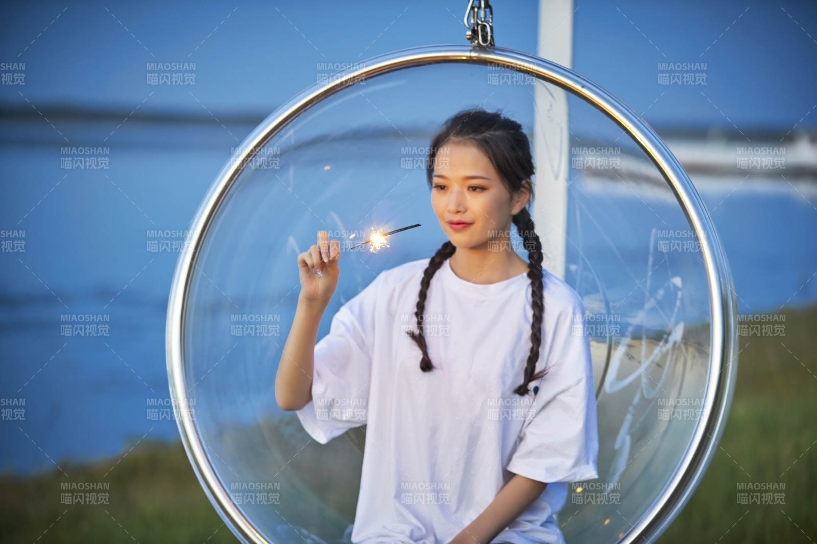 傍晚湖畔透明秋千上燃放仙女棒的可愛少女