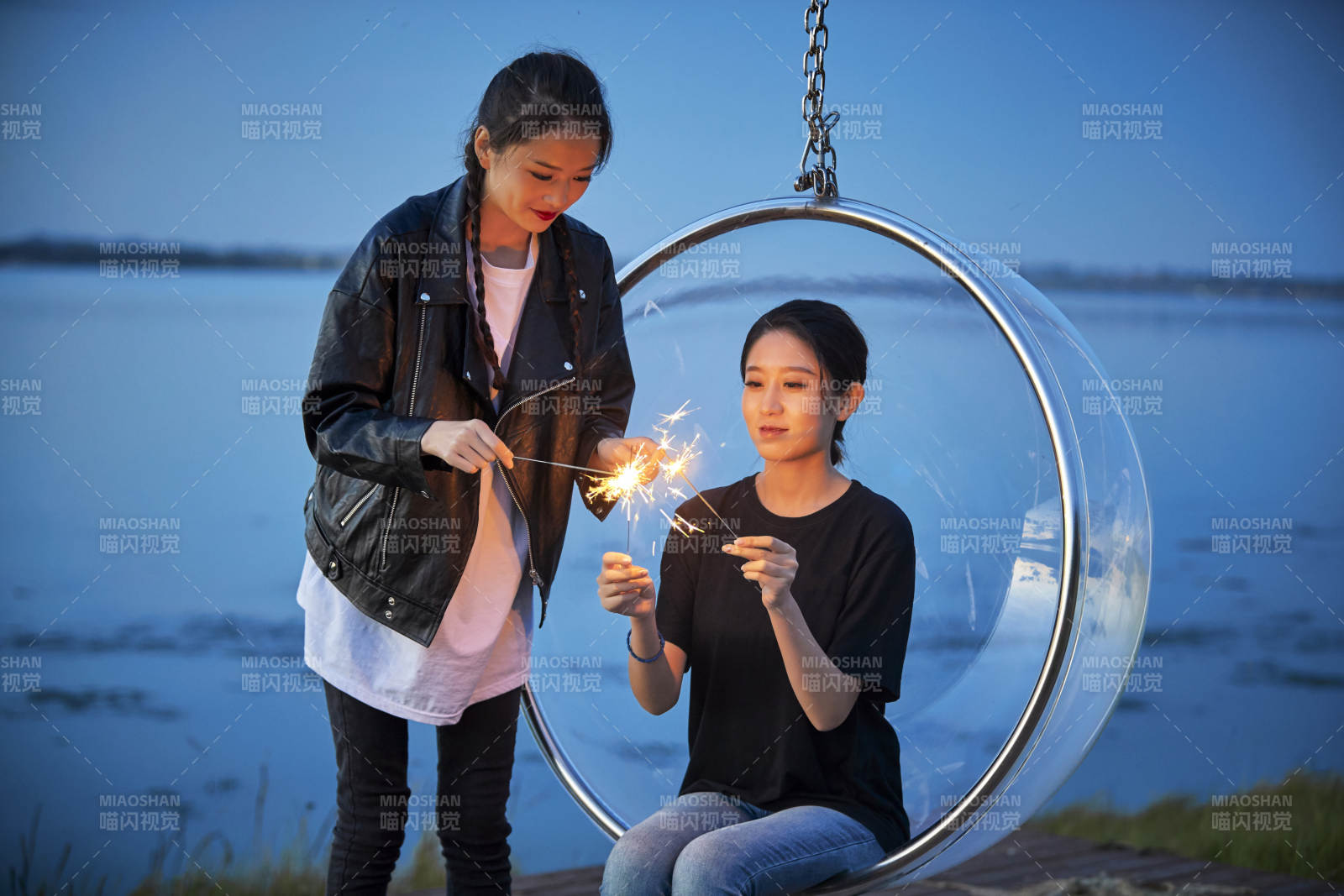 傍晚湖畔透明秋千上燃放仙女棒的可爱少女