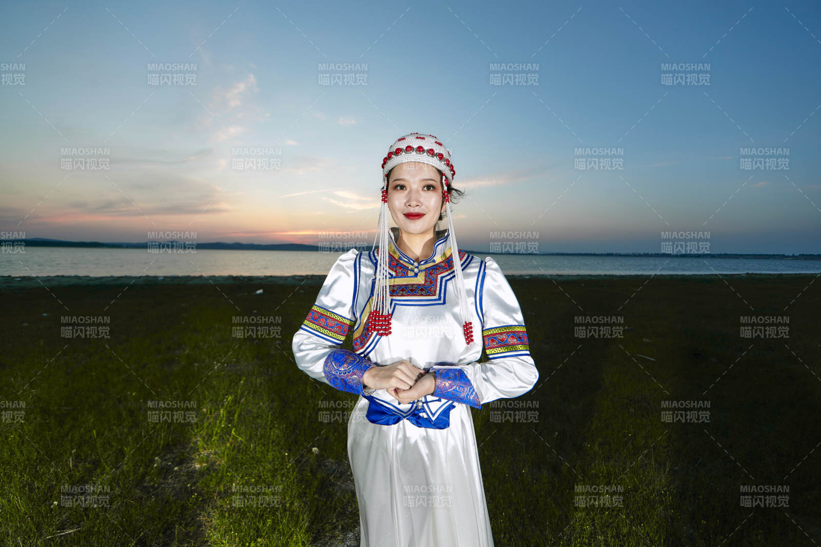 晚霞的草原湖畔穿蒙古族傳統服飾的年輕女性