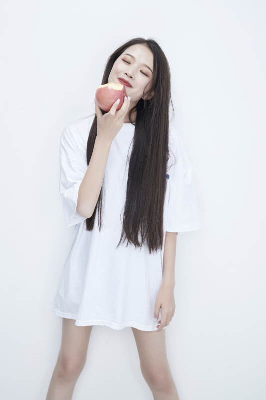 吃苹果的穿白色长T血衫的长发可爱少女人像