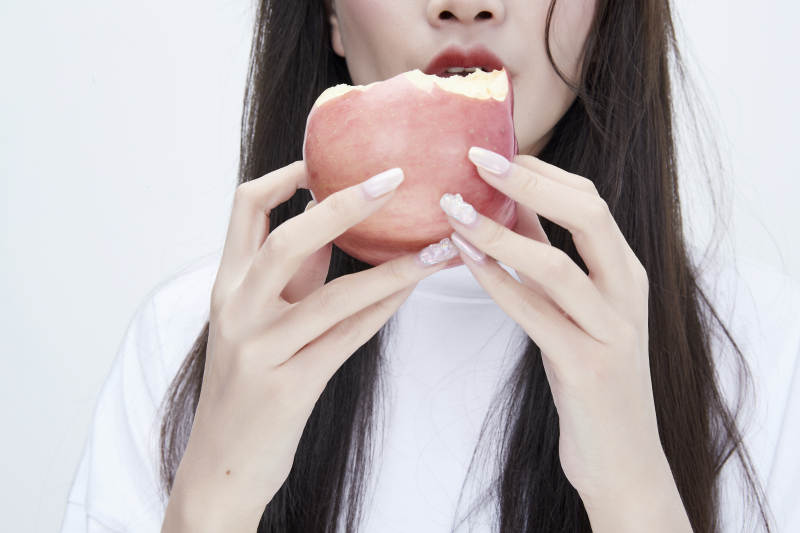 吃苹果的穿白色长T血衫的长发可爱少女人像