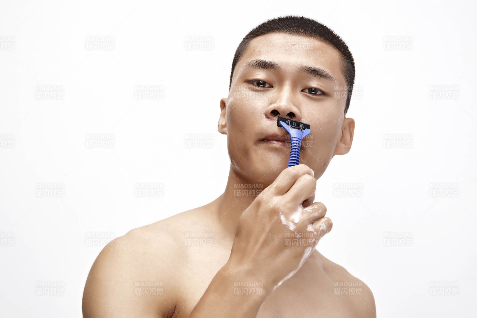 白色背景下手持剃须刀在刮胡子的亚洲男性