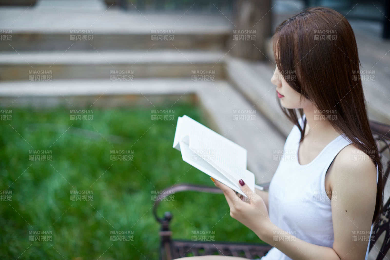 院子里坐在長椅上閱讀書籍的亞洲長發(fā)少女