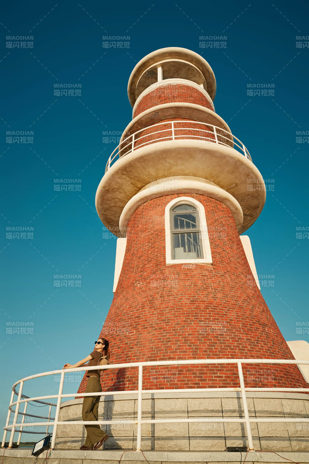 盛夏夕阳晚霞湖边码头灯塔上的少女