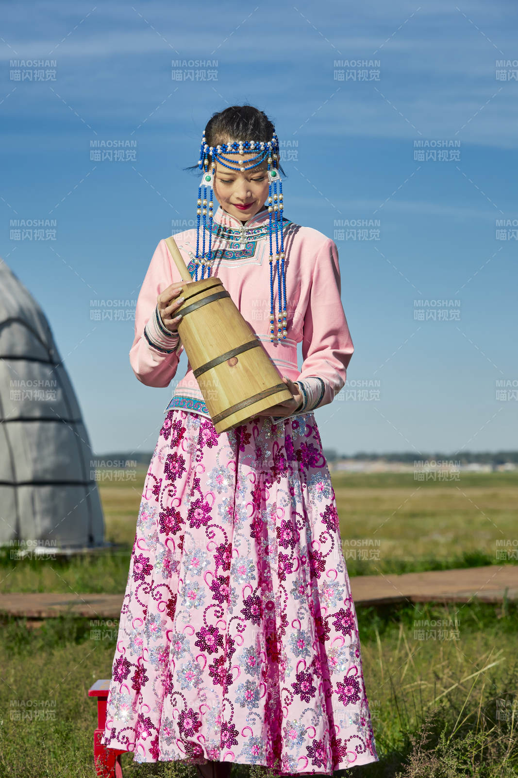 蒙古包前穿蒙古族飾懷抱奶茶桶的蒙族少女
