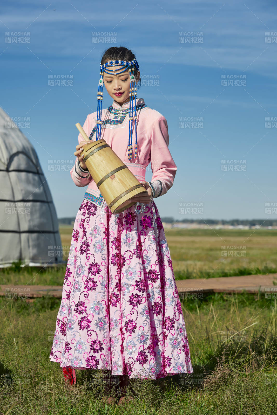 蒙古包前穿蒙古族飾懷抱奶茶桶的蒙族少女