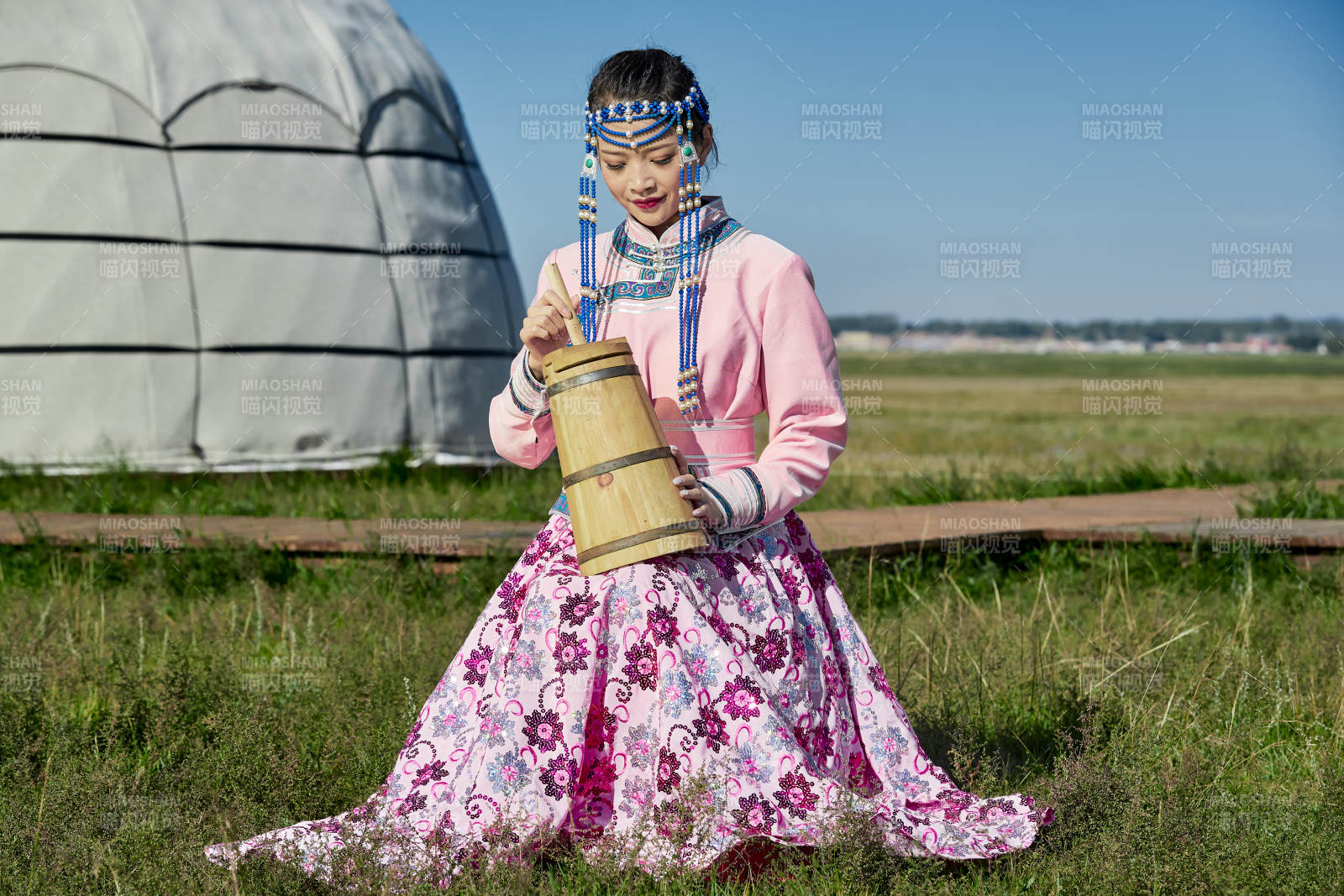 蒙古包前穿蒙古族飾懷抱奶茶桶的蒙族少女